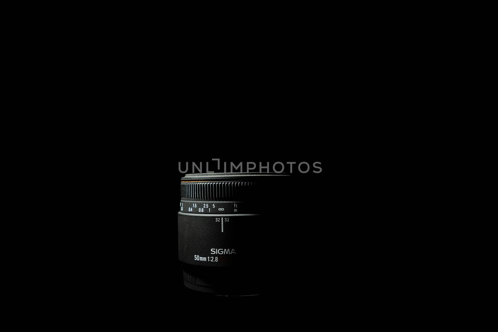 Ukraine; Kyiv; 20.02.2019 Sigma 50mm f1:2,8 DG EX Macro lens. Underexposed photo of DSLR camera lens lying on black background. Stock photo isolated. Low light photo and large depth of field.