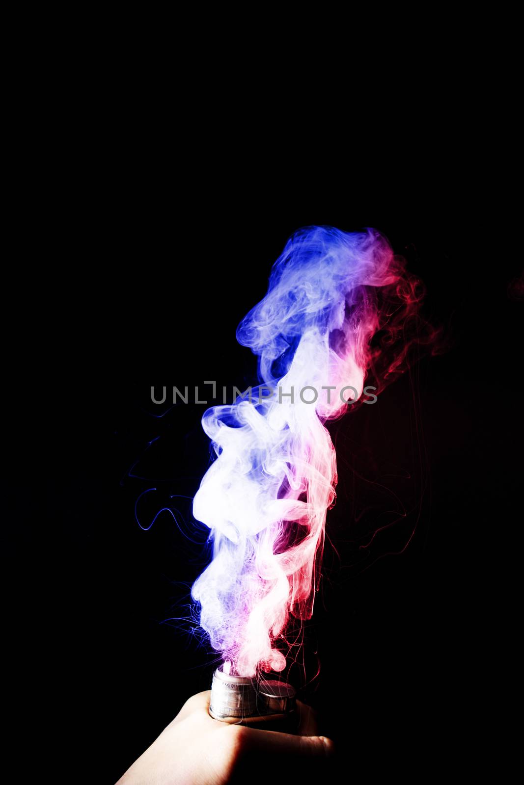Male hand holds vape. Vape clouds splash from vape coil on black background. Fog is dual color — blue and red. Stock isolated dual colour smoke with spray boiling glycerine.