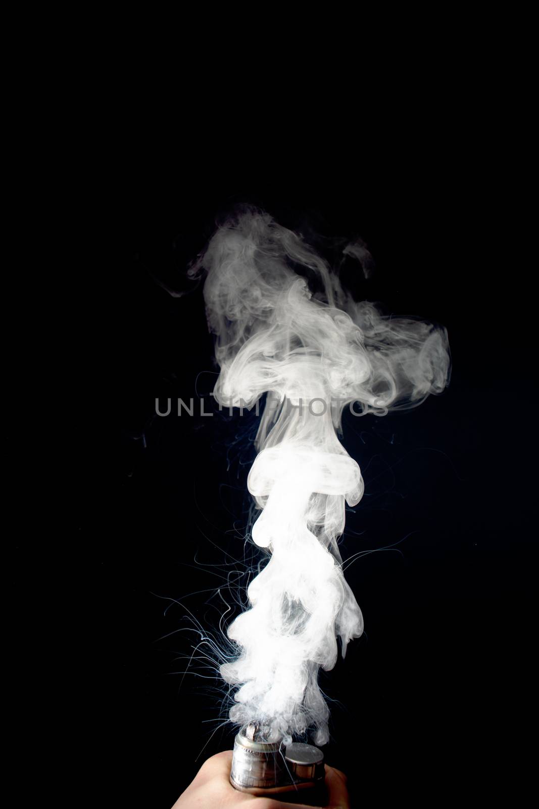 Male hand holds vape without atomiser. Column of vape clouds splash from coil on black background. Fog is white. Stock isolated white smoke with spray boiling glycerine.