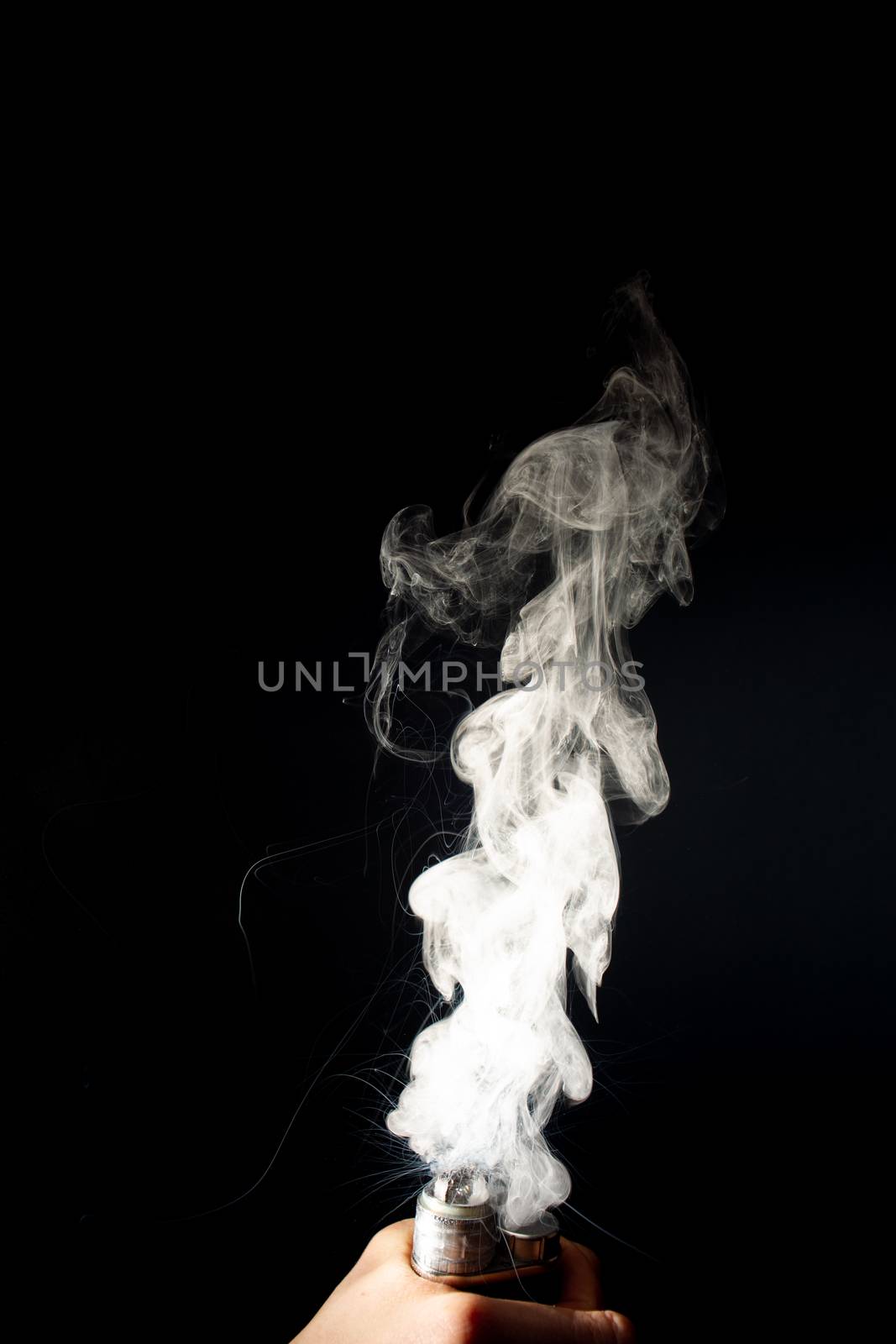 Man hand holds vape. Vape clouds splash from coil on black background. Fog is white. Stock isolated white smoke with spray boiling glycerine around.
