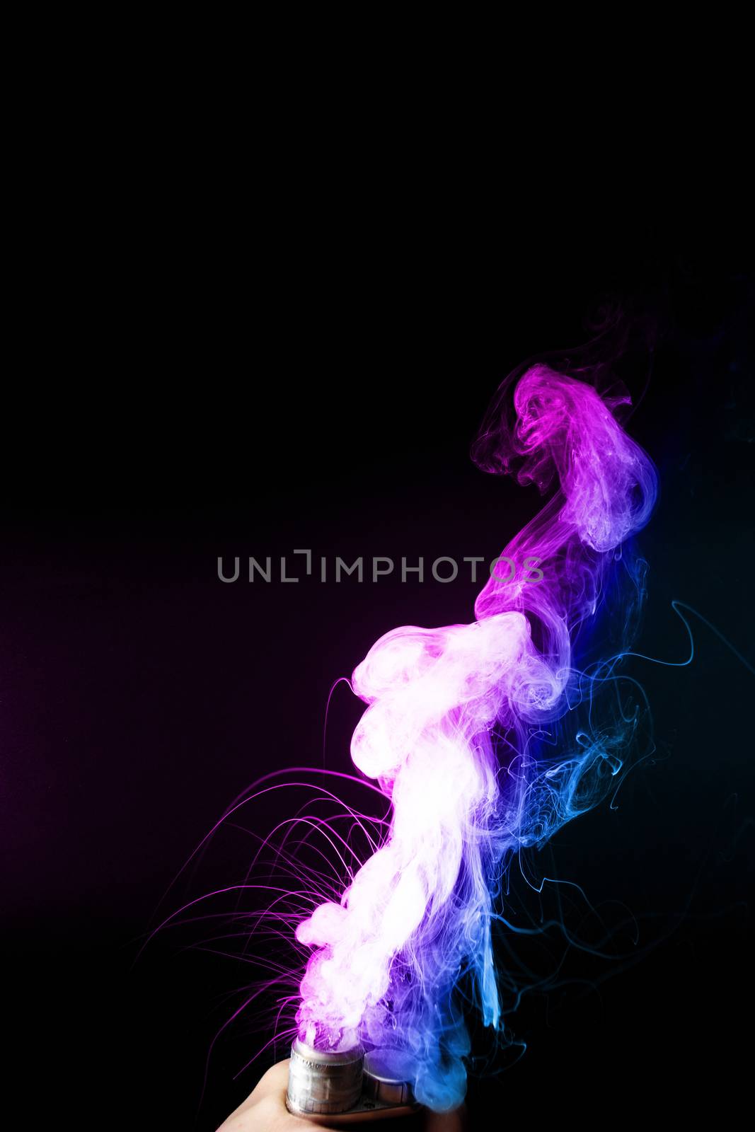 Male hand holds vape. Vape clouds splash from vape coil on black background. Fog is dual color — blue and purple. Stock isolated colorful smoke with spray boiling glycerine.
