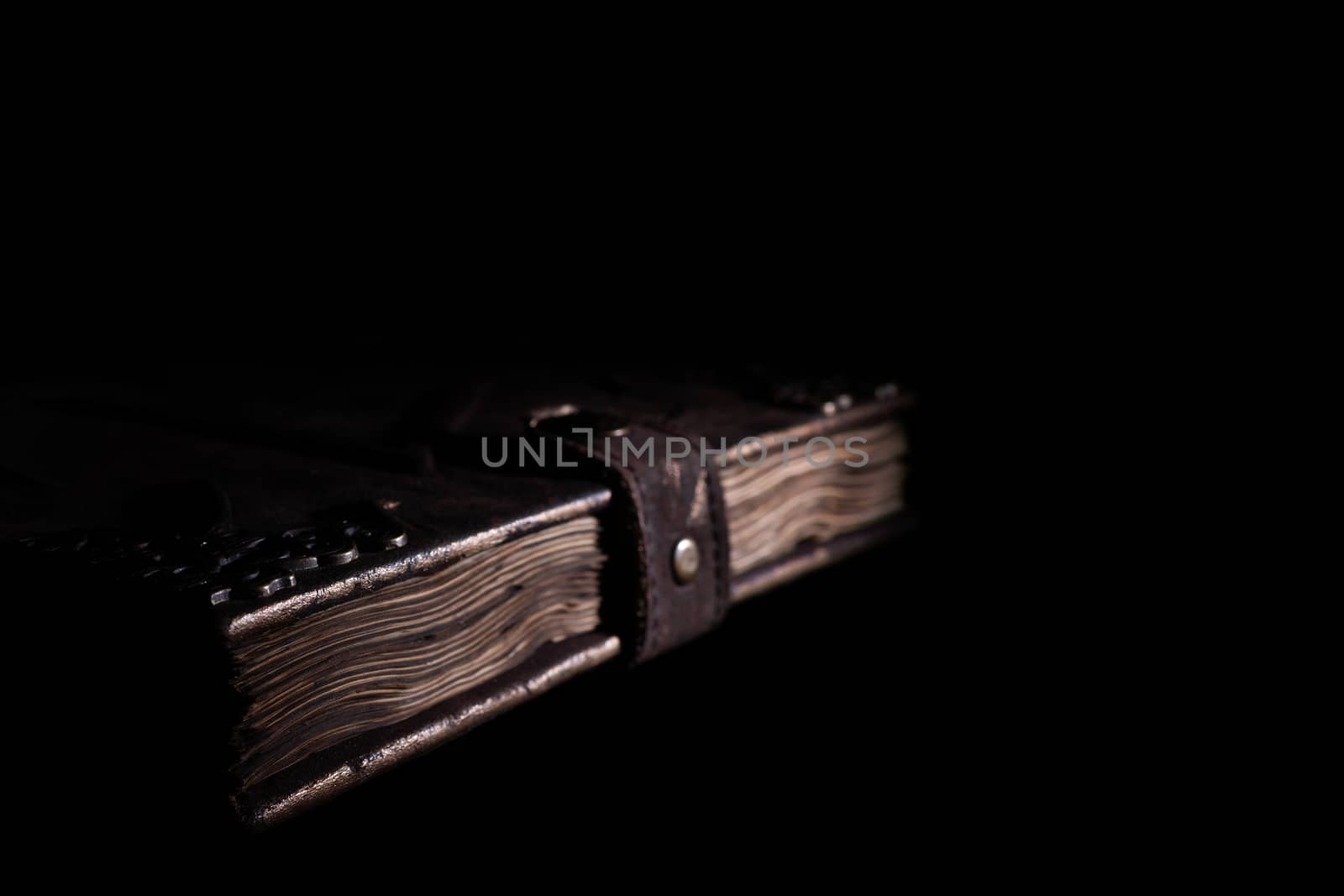 Handmade old leather cover notebook. Charred sheets and leather clasp isolated on black background. Underexposed stock photo.