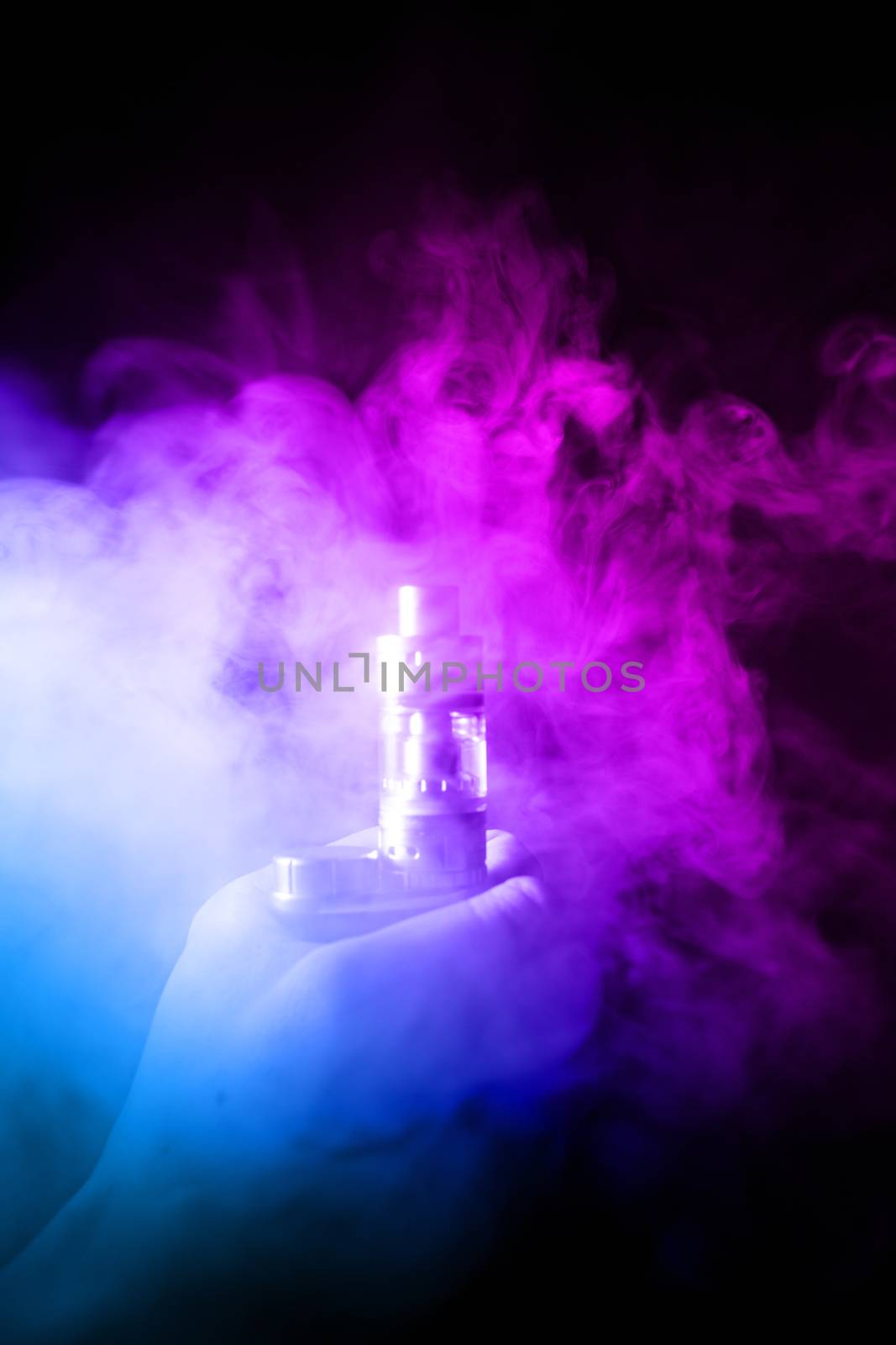 Male hand holds vape in thick vape fog or smoke. Vape clouds around hand with vape on black background. Fog is dual color — blue and purple. Stock isolated colorful smoke with spray glycerine.
