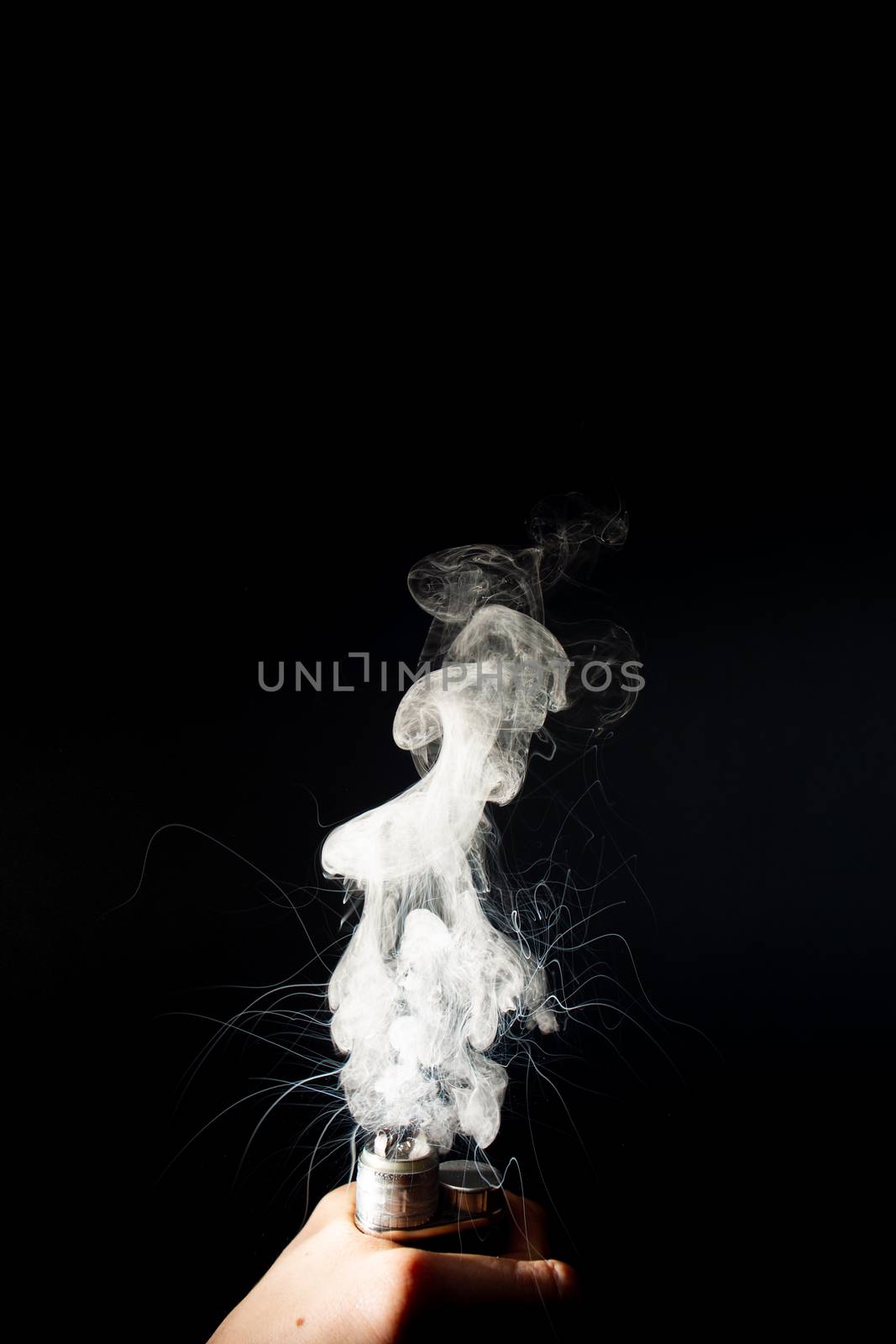 Man hand holds vape. Vape clouds splash from coil on black background. Fog is white. Stock isolated white smoke with spray boiling glycerine around.