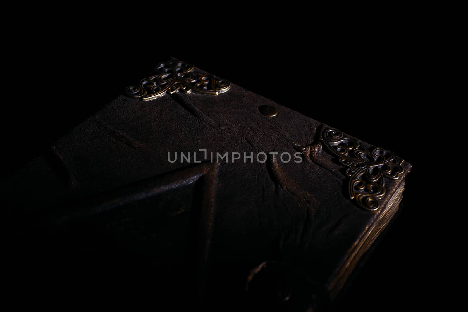 Low light old handmade leather cover notebook. Old leather cover and charred sheets isolated on black background. Underexposed stock photo.
