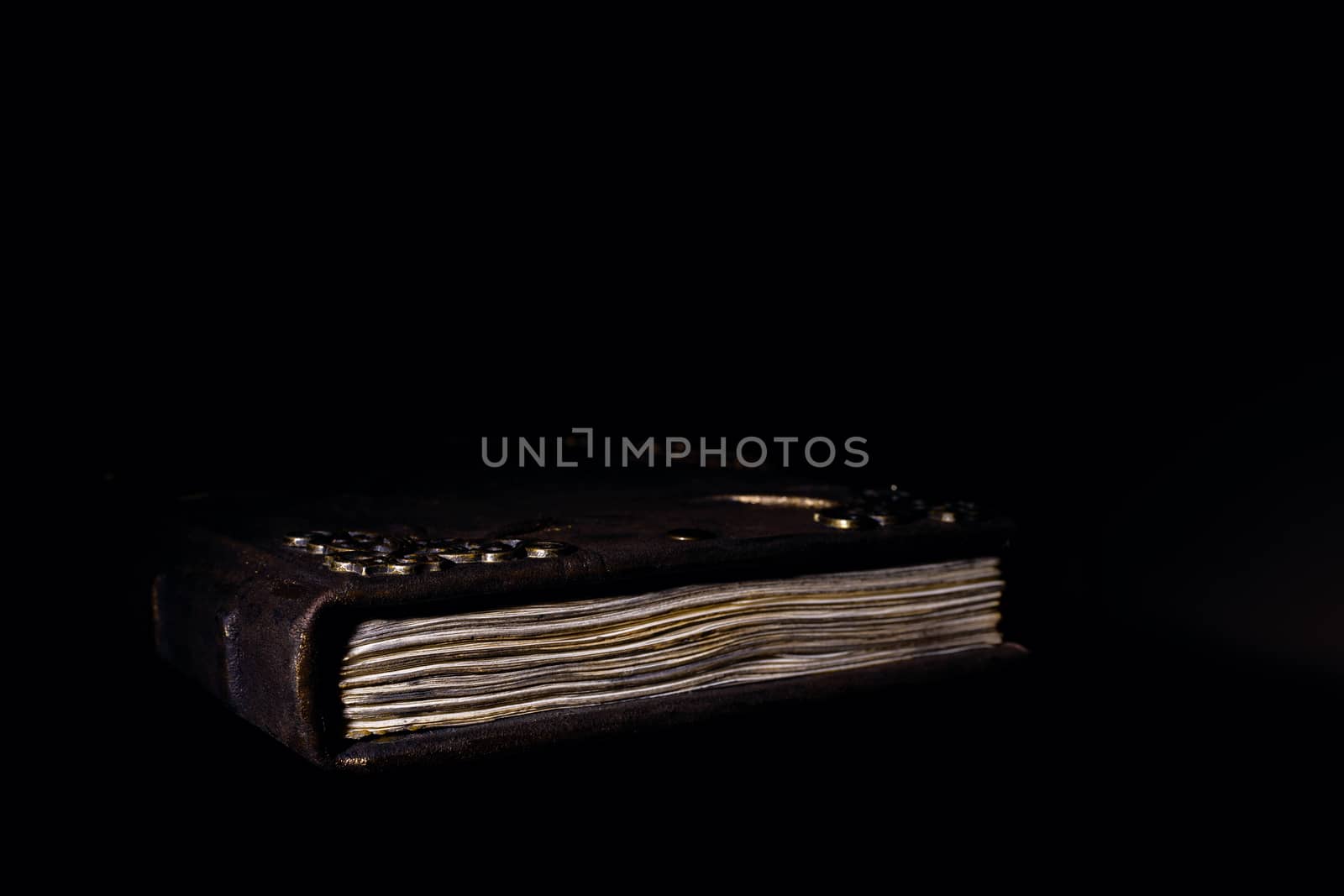 Low light old handmade leather cover notebook. Old leather cover and charred sheets isolated on black background. Underexposed stock photo.