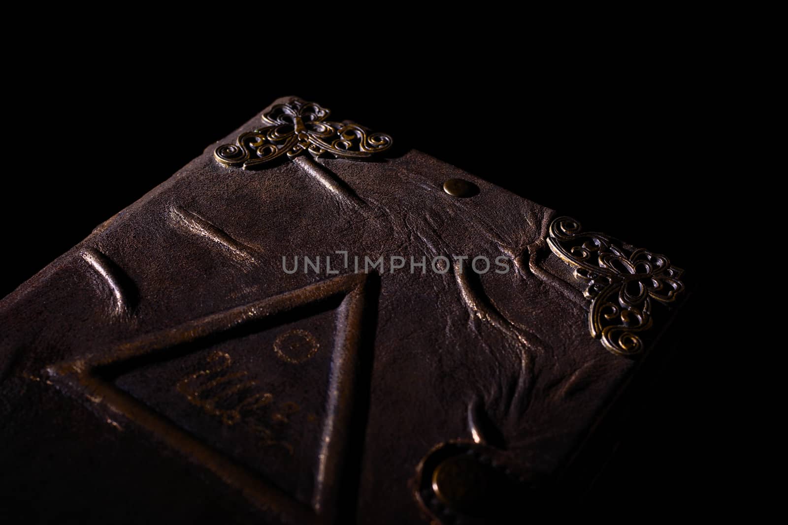 Low light handmade old leather cover notebook. Charred sheets and cover isolated on black background. Underexposed stock photo.