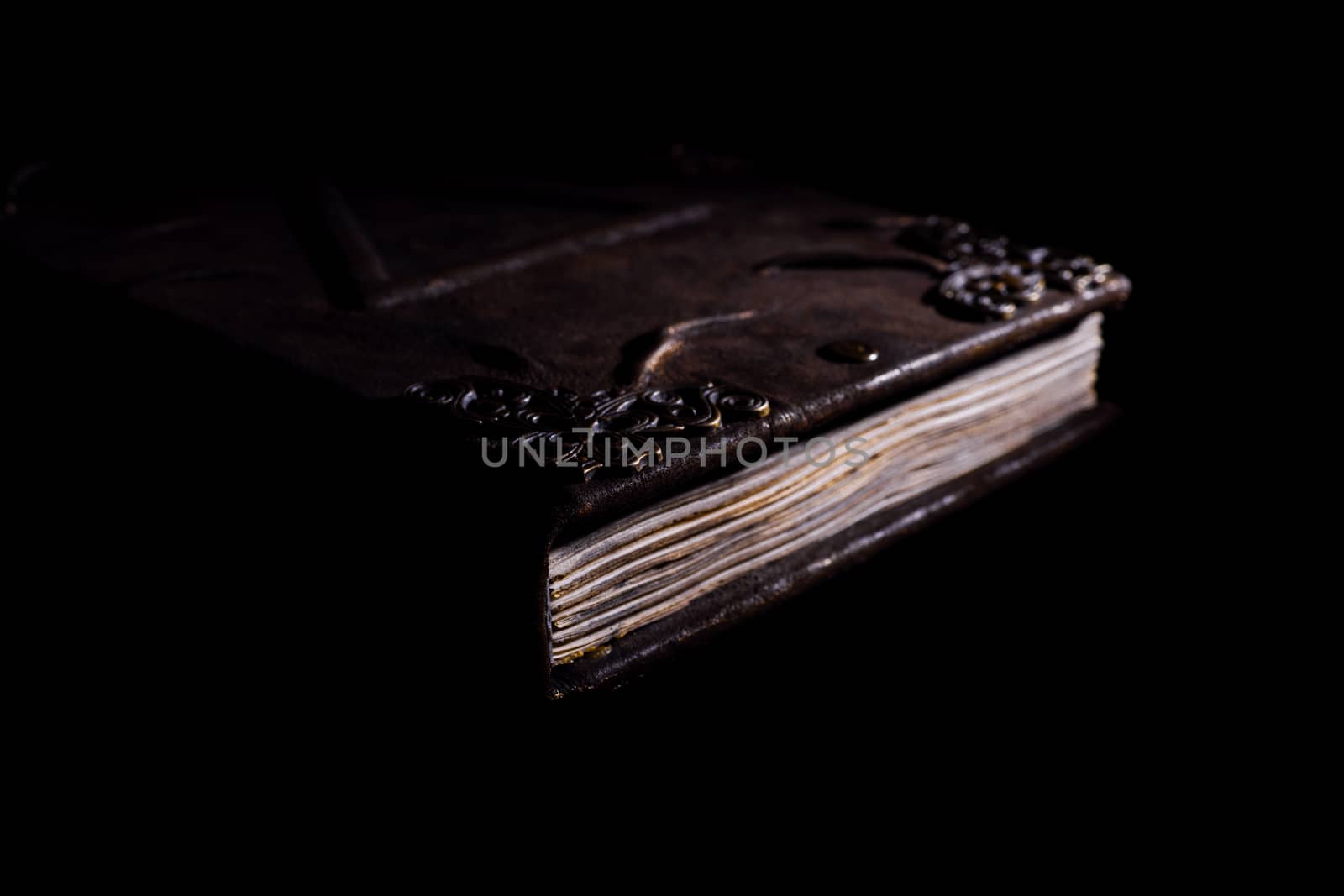 Low light old handmade leather cover notebook. Old leather cover and charred sheets isolated on black background. Underexposed stock photo.
