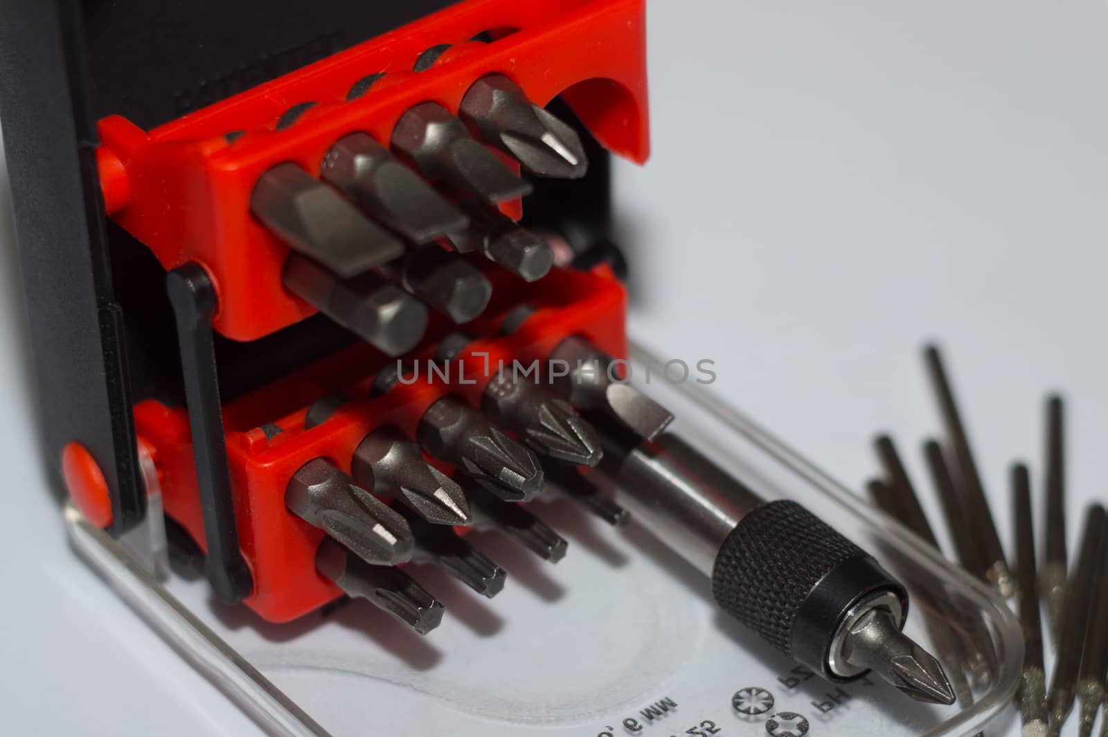 Bits holder in box and many tool bits on white background. Close-up view. Red element in plastic box.