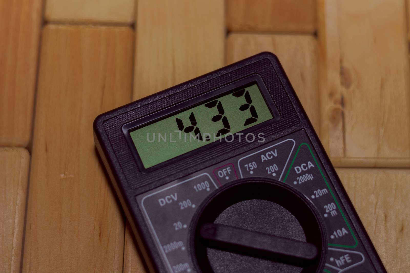 Digital measuring multimeter on wooden floor. It shows 4.33V or fully charged battery. Includes voltmeter, ampermeter, ohmmeter.