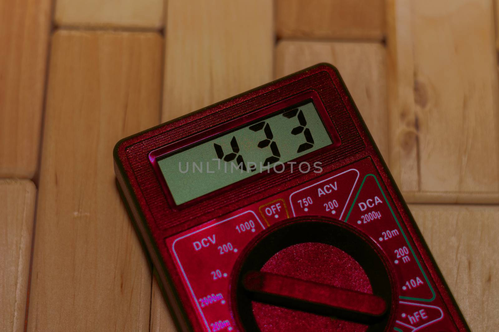Red digital measuring multimeter on wooden floor. It shows 4.33V or fully charged battery. Includes voltmeter, ampermeter, ohmmeter.