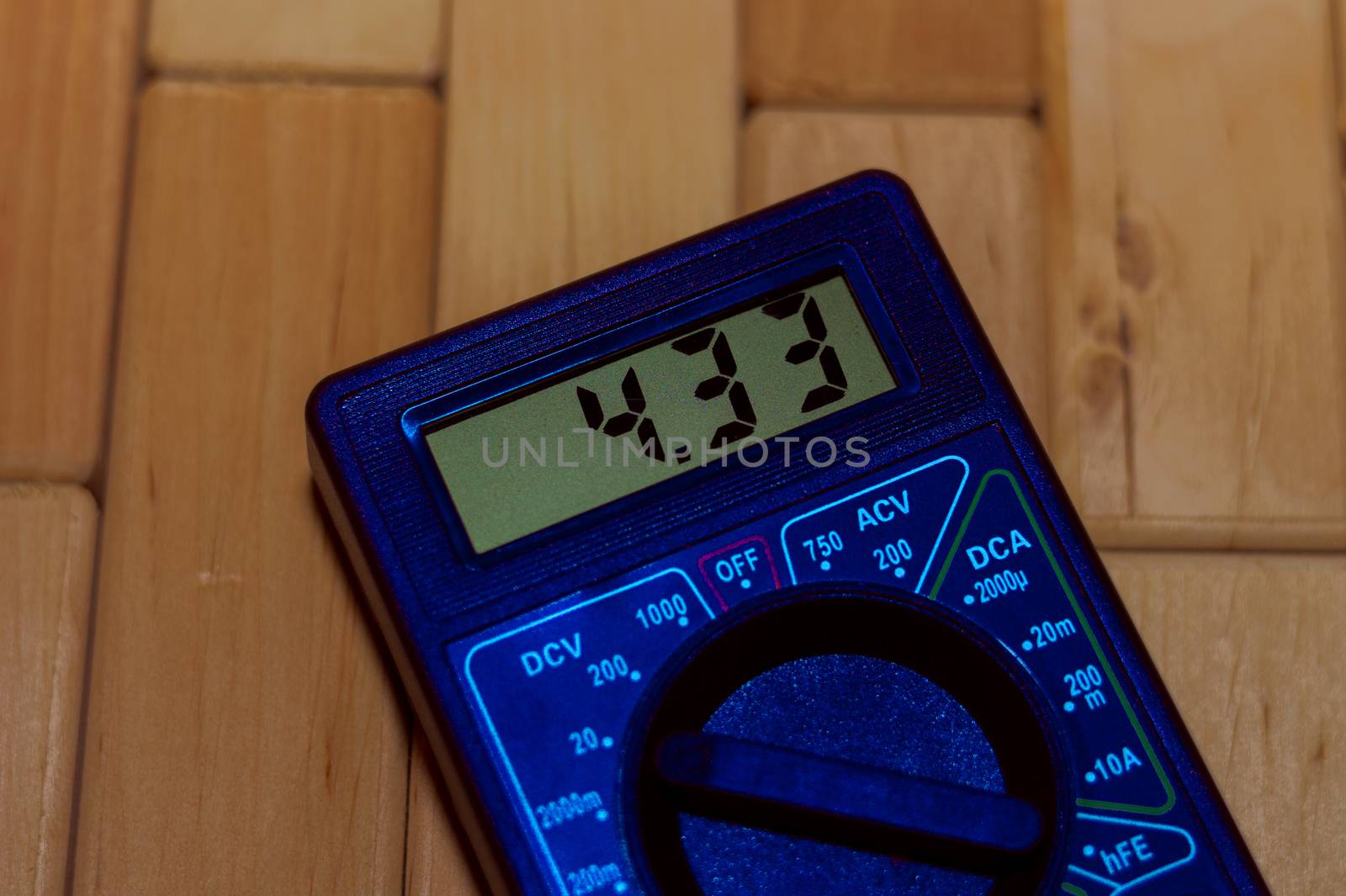 Blue digital measuring multimeter on wooden floor. It shows 4.33V or fully charged battery. Includes voltmeter, ampermeter, ohmmeter.