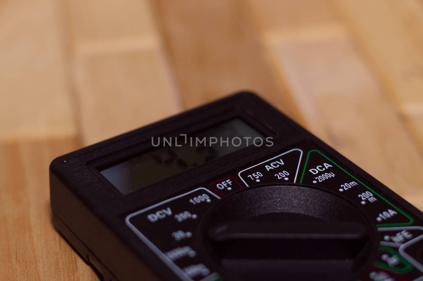 Digital measuring multimeter on wooden floor. It shows 4.33V or fully charged battery. Includes voltmeter, ampermeter, ohmmeter.