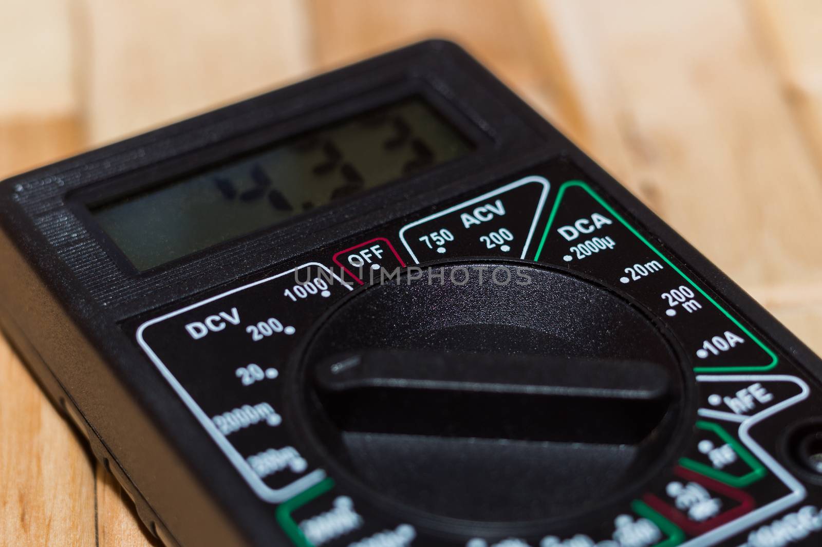 Digital measuring multimeter on wooden floor. It shows 4.33V or fully charged battery. Includes voltmeter, ampermeter, ohmmeter.