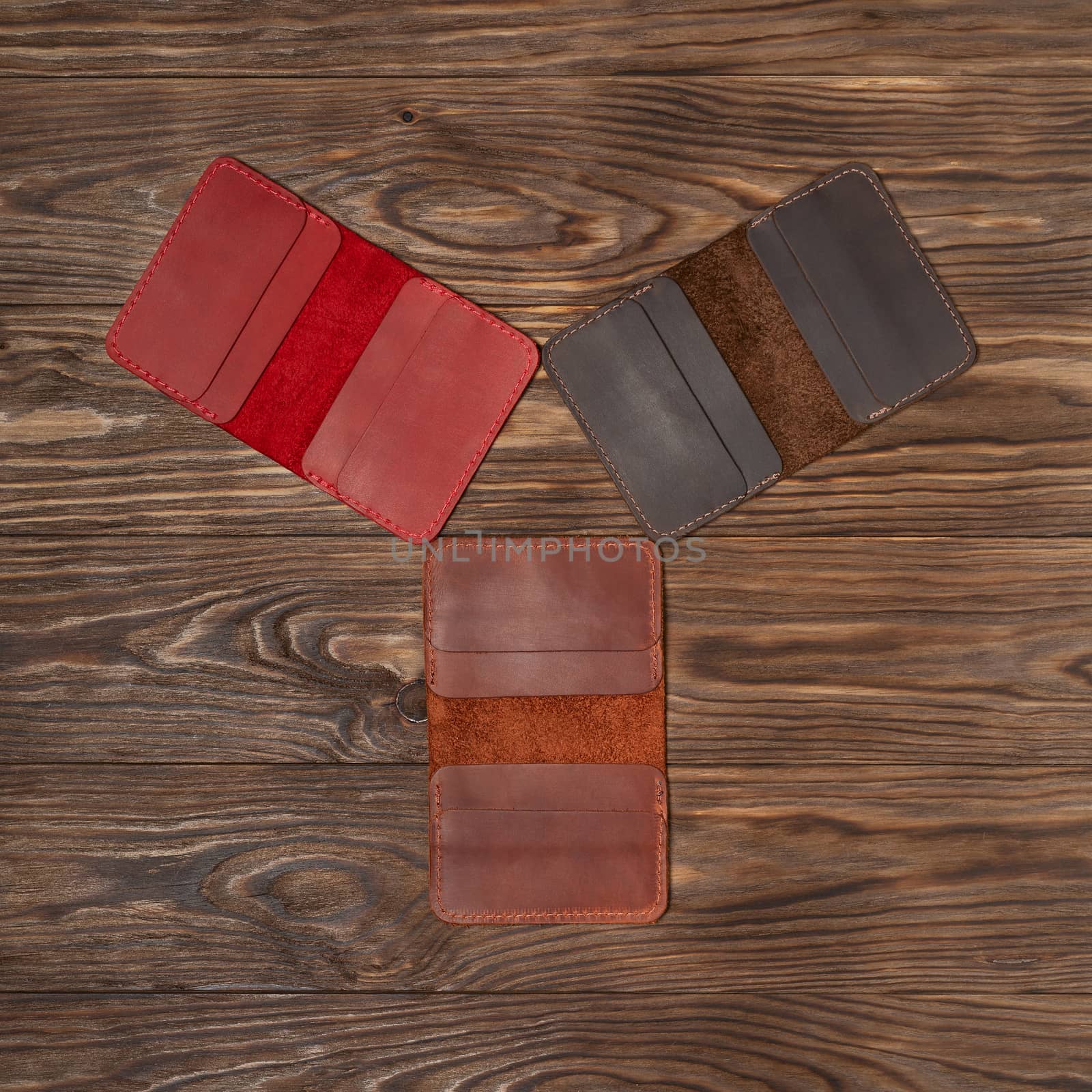 Tree handmade different colour leather cardholders on wooden background. Stock flat lay photo. Red, ginger and brown cardholders on photo.