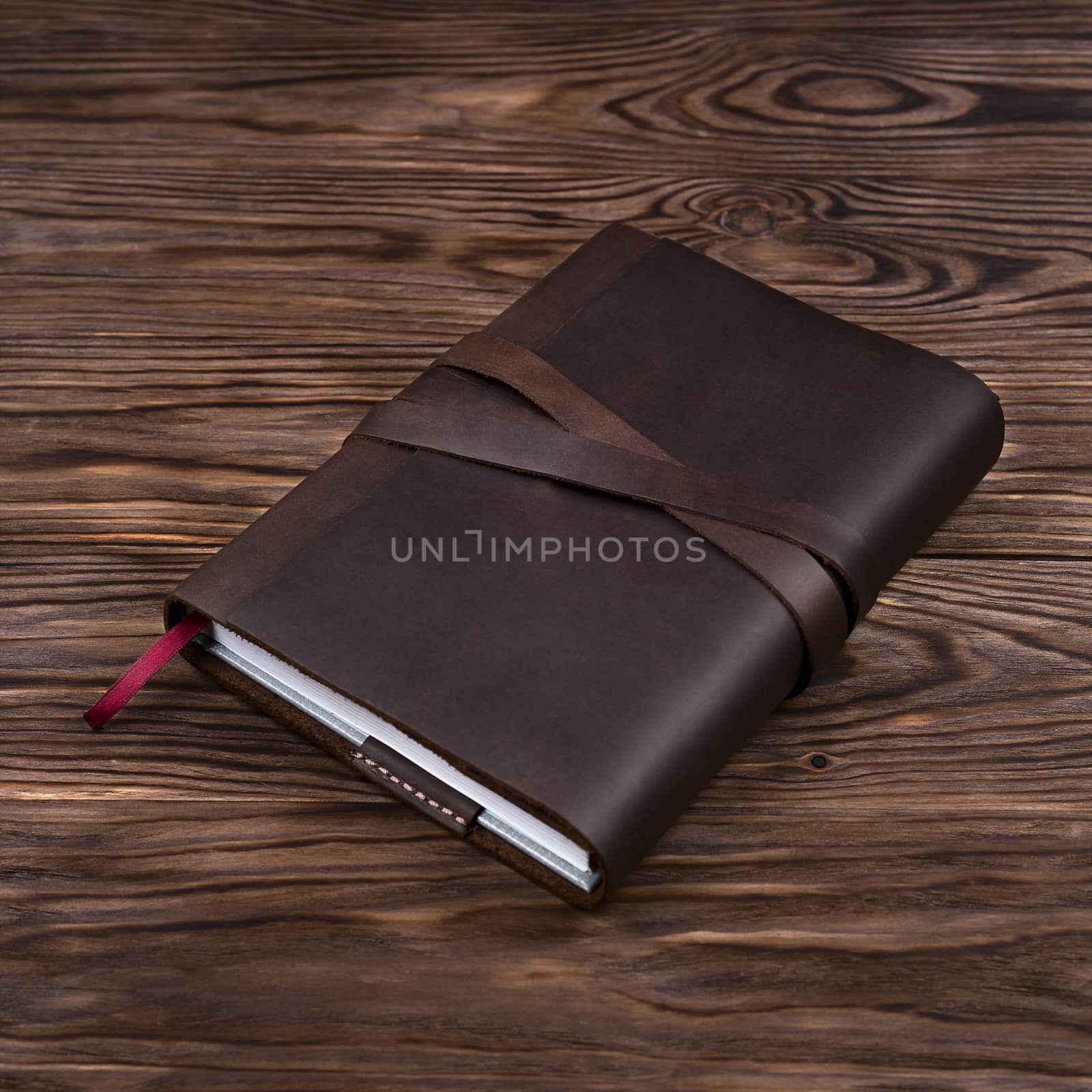 Brown handmade leather notebook cover with notebook inside on wooden background. Stock photo of luxury business accessories.