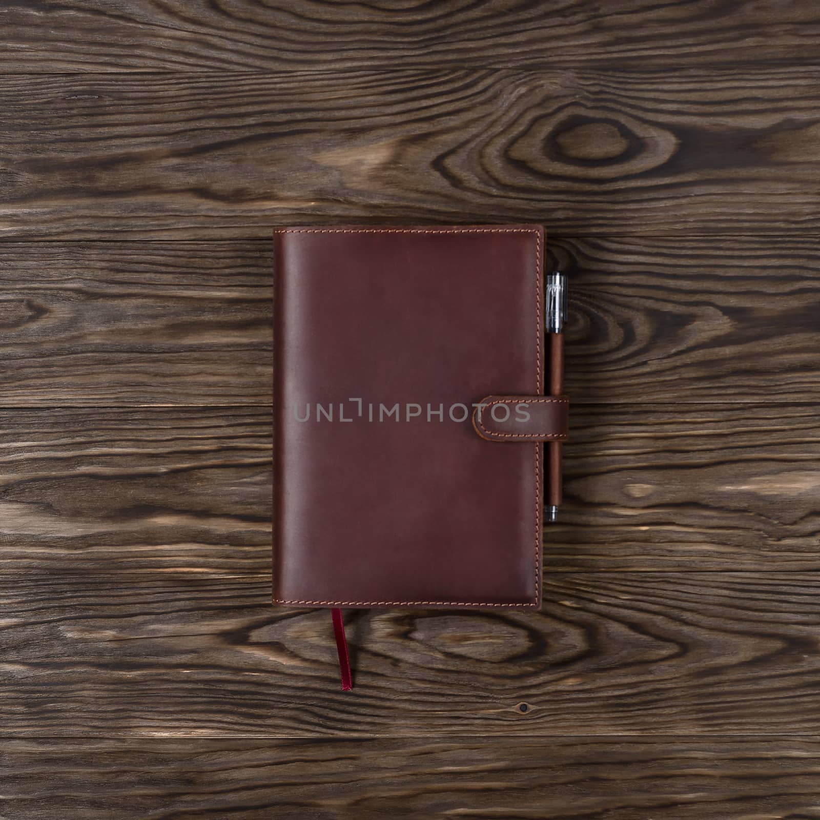 Brown handmade leather notebook cover with notebook and pen on wooden background. Stock photo of luxury business accessories. Up to down view.