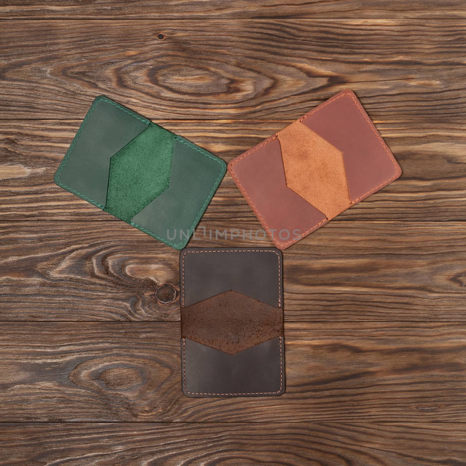 Tree handmade different colour leather cardholders on wooden background. Stock flat lay photo. Green, ginger and brown cardholders on photo.