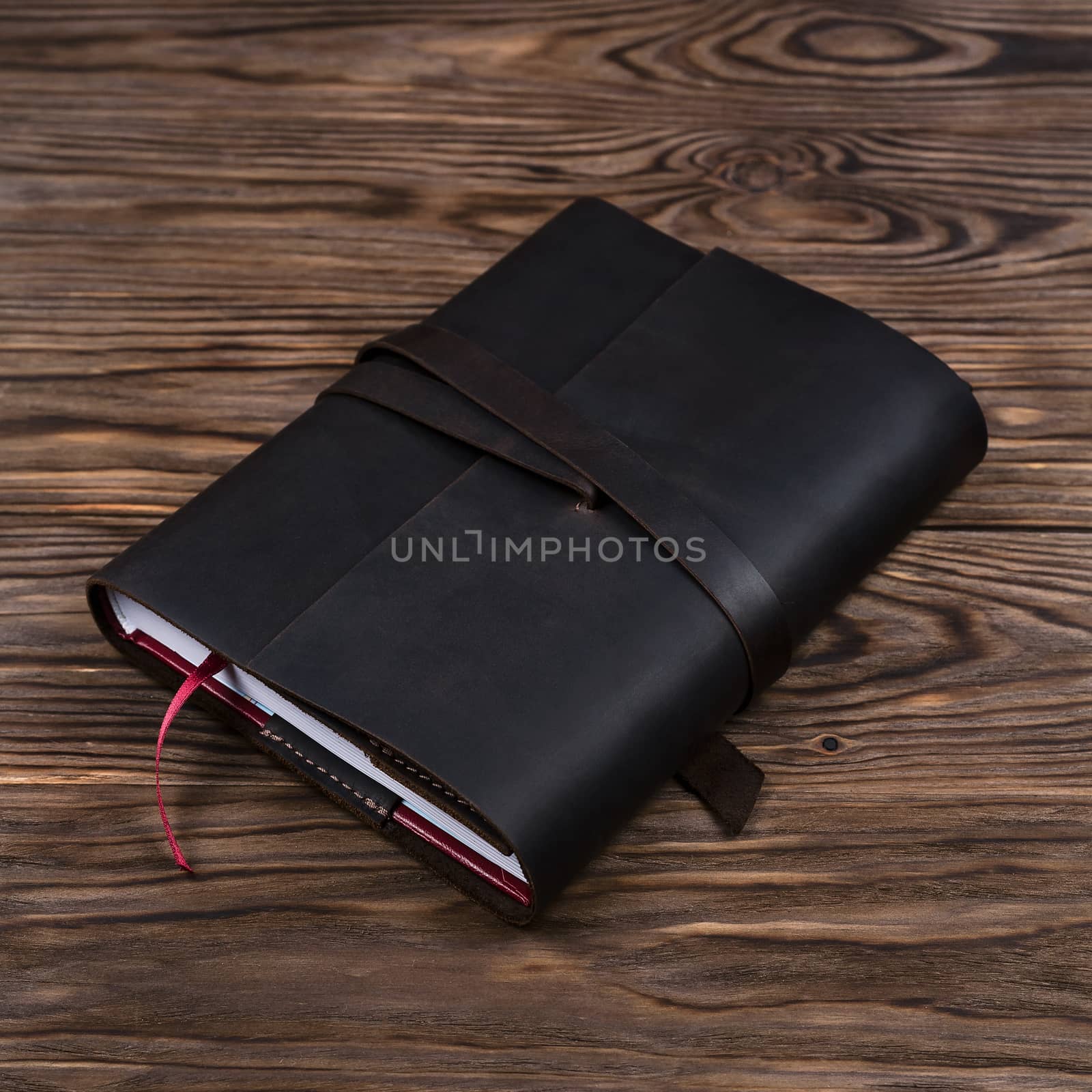 Black handmade leather notebook cover with notebook inside on wooden background. Stock photo of luxury business accessories.