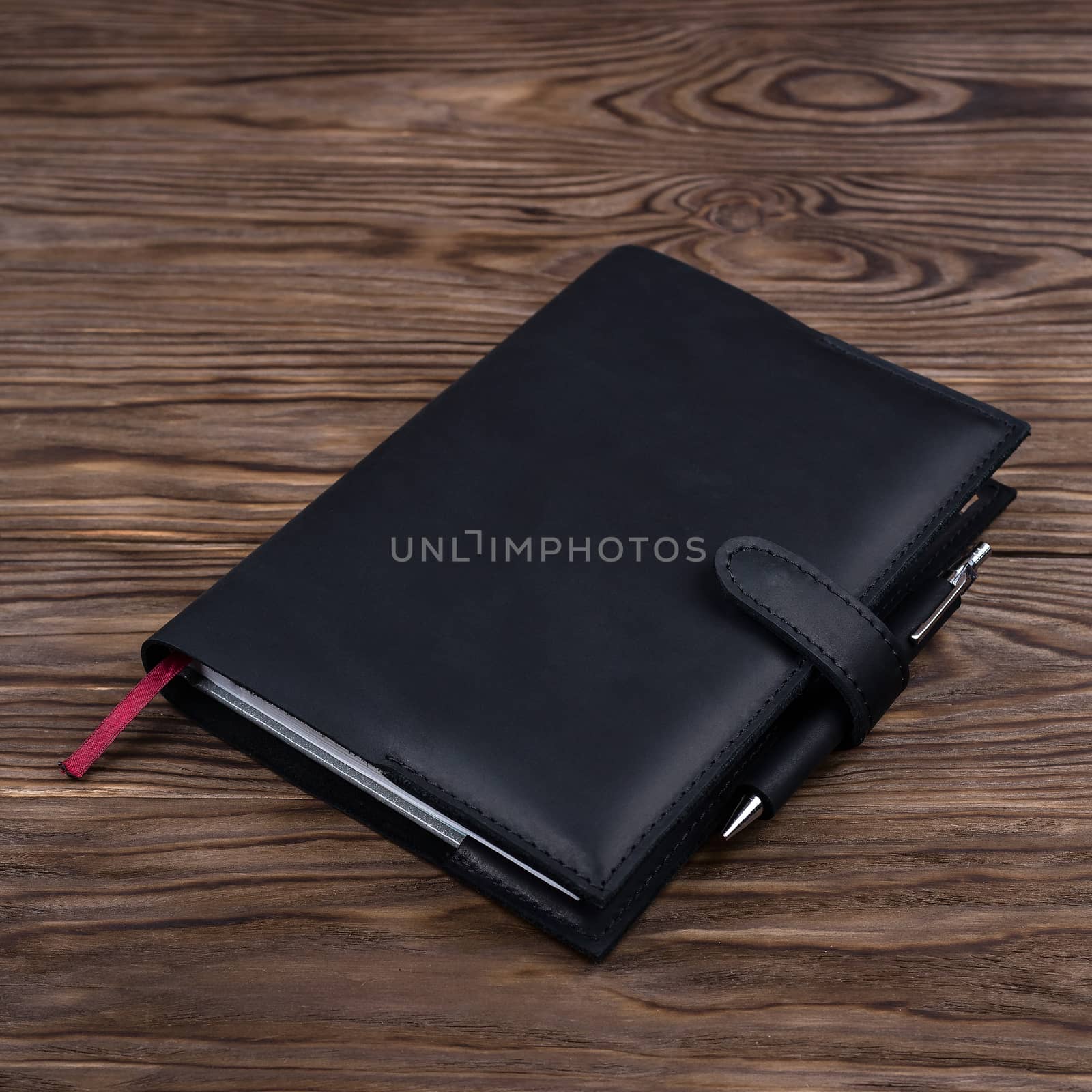 Black handmade leather notebook cover with notebook and pen inside on wooden background. Stock photo of luxury business accessories. by alexsdriver