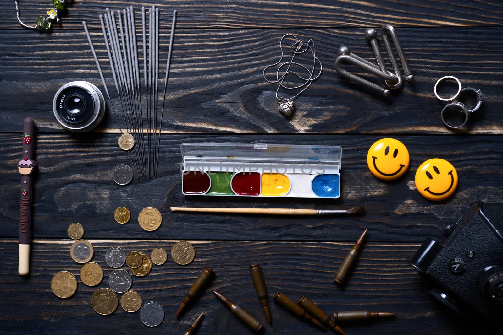 Flat lay wooden charred background. On wooden boards lies bengali fire, silver pendant, rings, coins, pen, brush and paint, ammo, camera prism and old lens