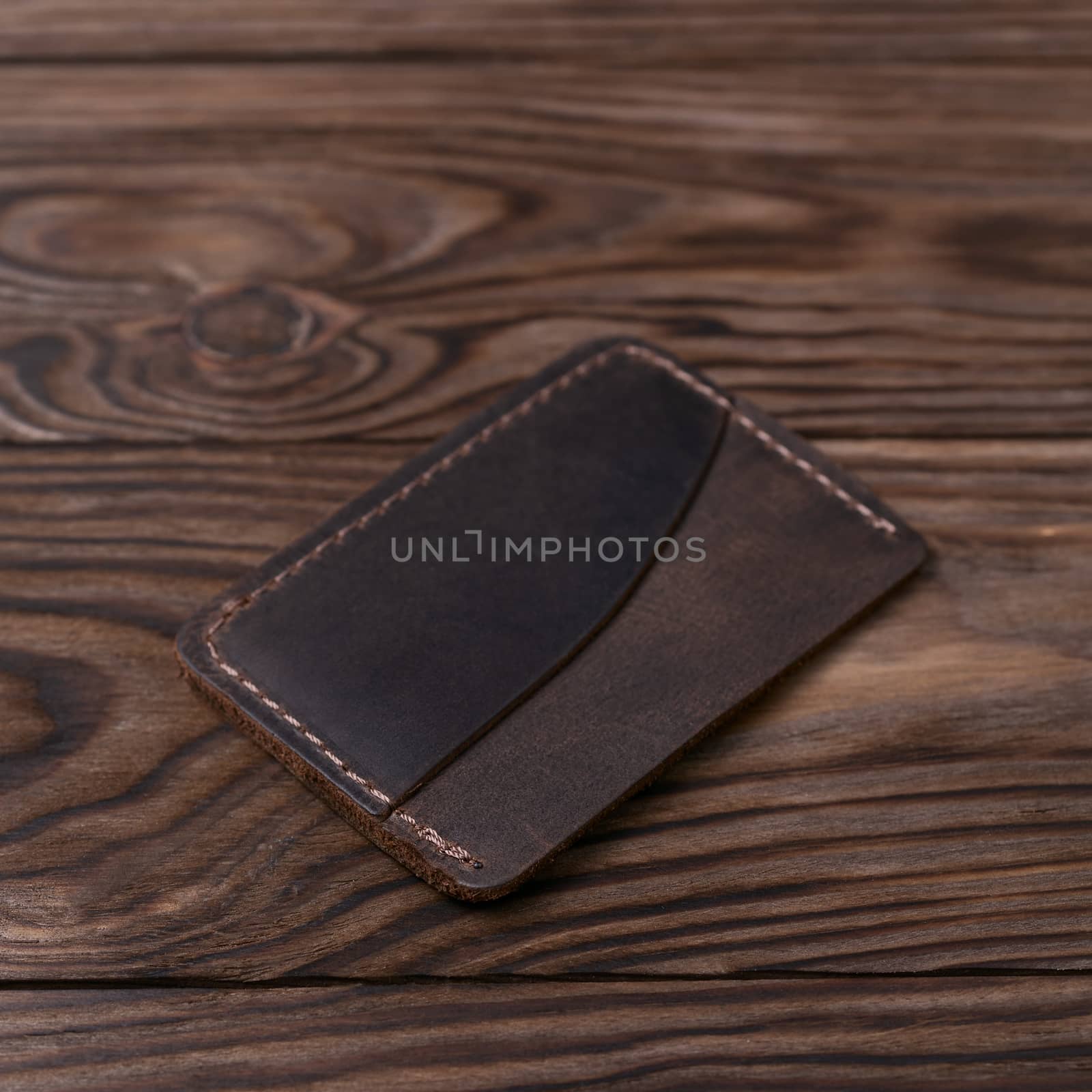Brown colour handmade leather one pocket cardholder on wooden background. Stock photo with soft blurred background. by alexsdriver