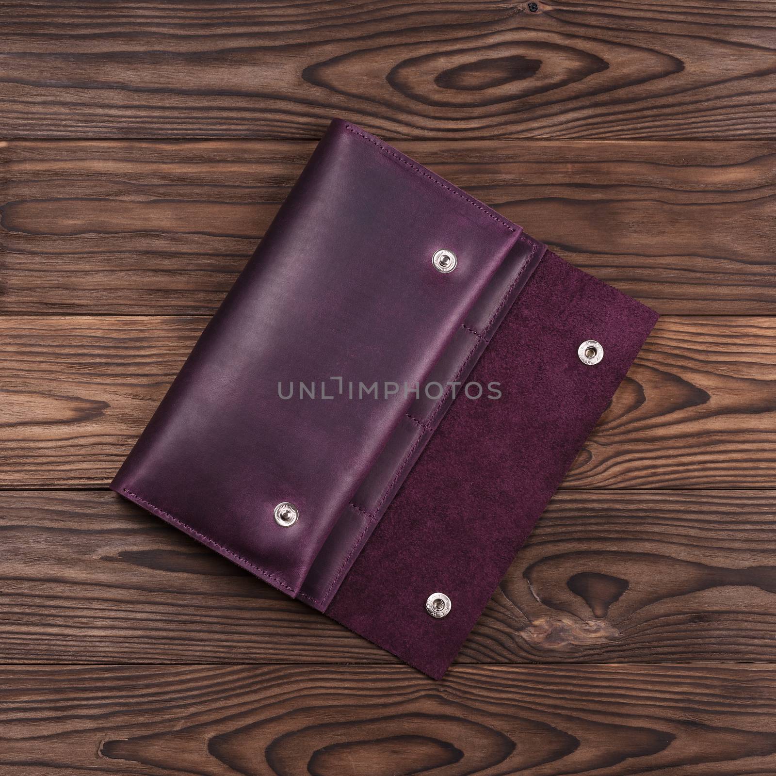 Purple handmade travel wallet lies on textured wooden backgroud closeup. Up to down view. Stock photo of businessman accessories. by alexsdriver