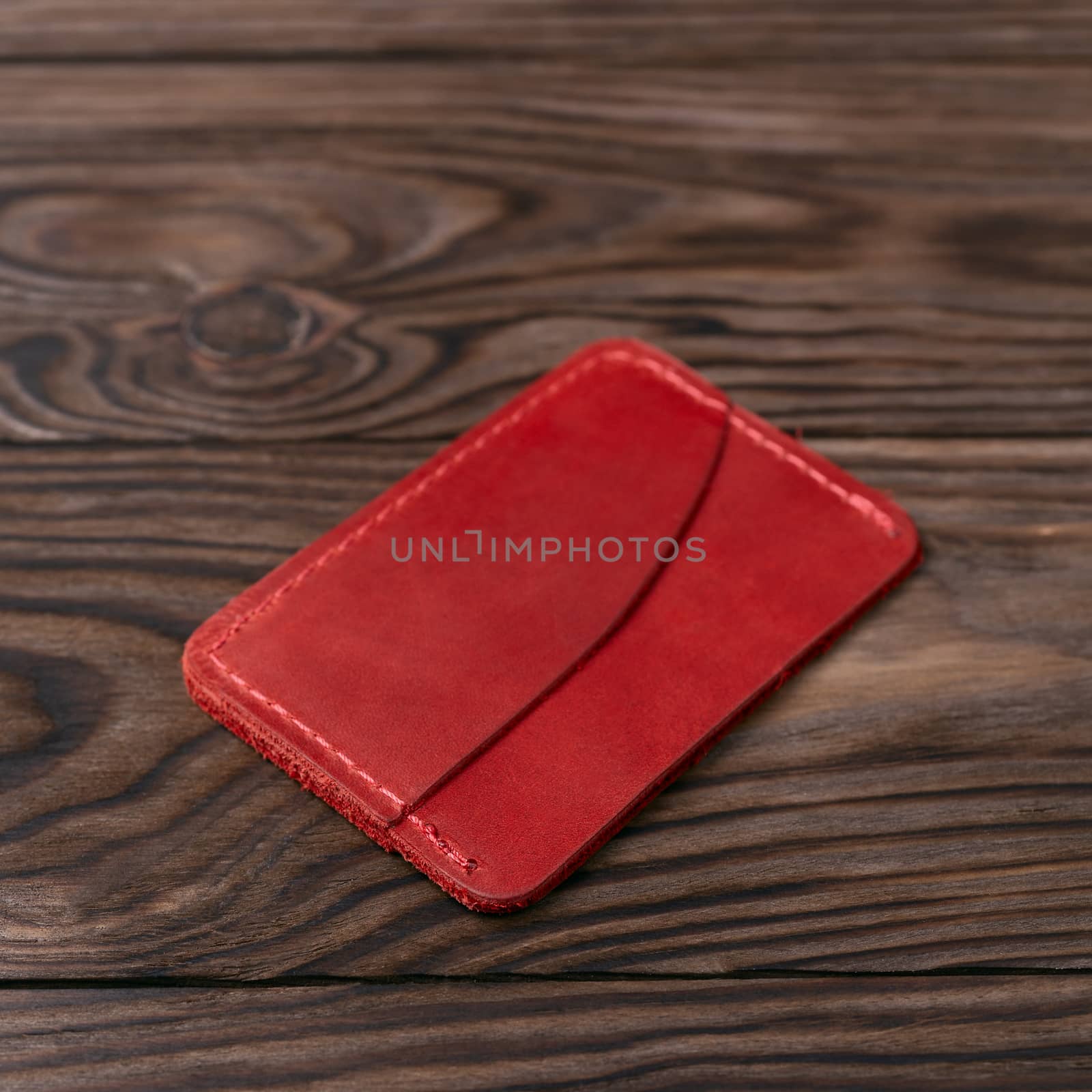 Red colour handmade leather one pocket cardholder on wooden background. Stock photo with soft blurred background.