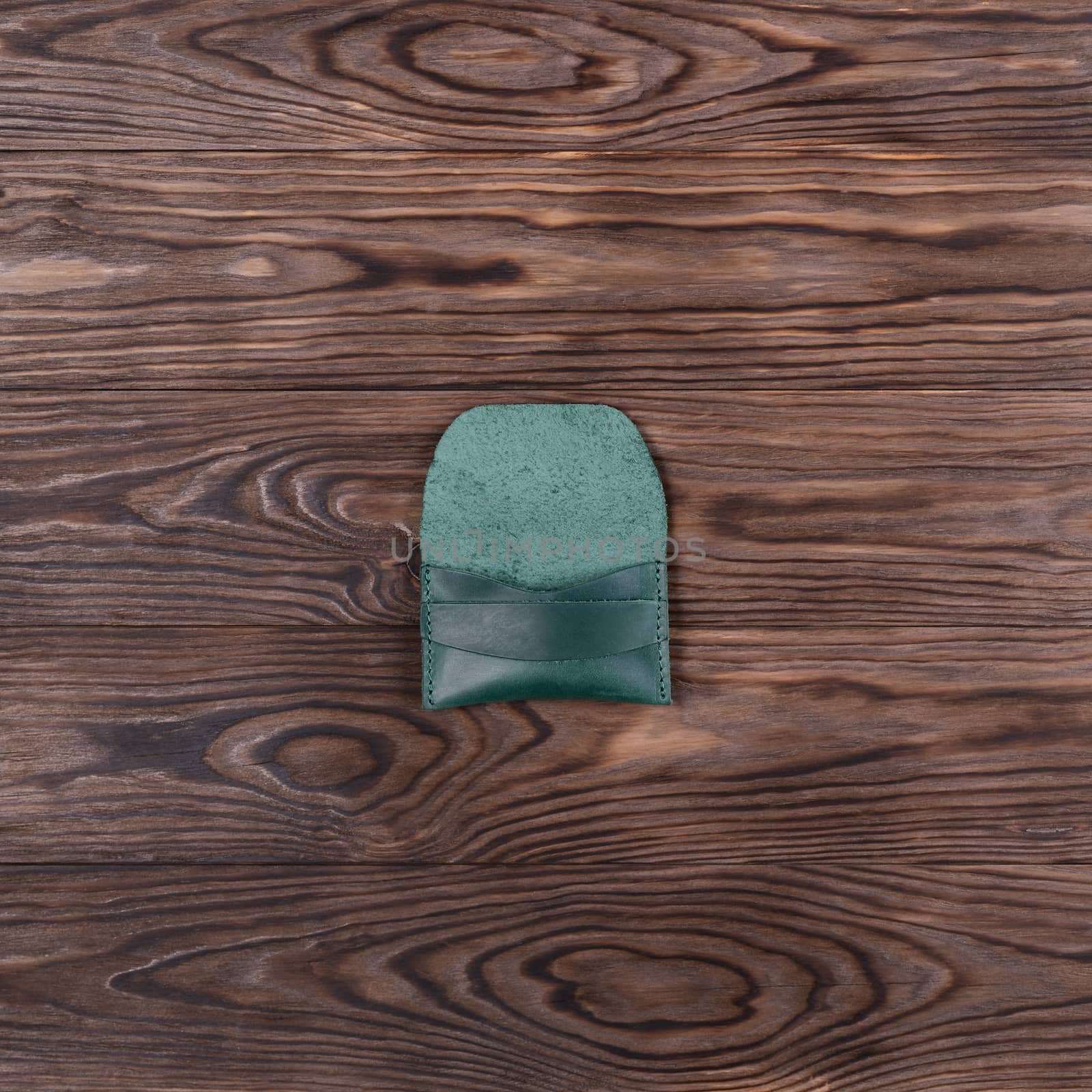 Flat lay photo of green colour handmade leather one pocket cardholder. Stock photo on wooden background.