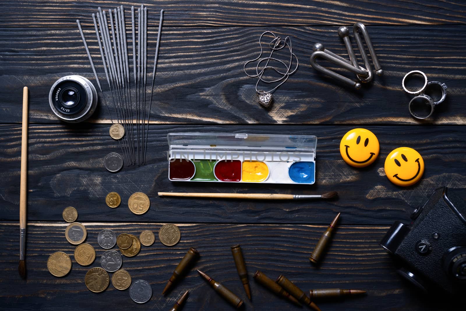 Flat lay wooden charred background. On wooden boards lies bengali fire, silver pendant, rings, coins, brush and paint, ammo, camera prism and old lens