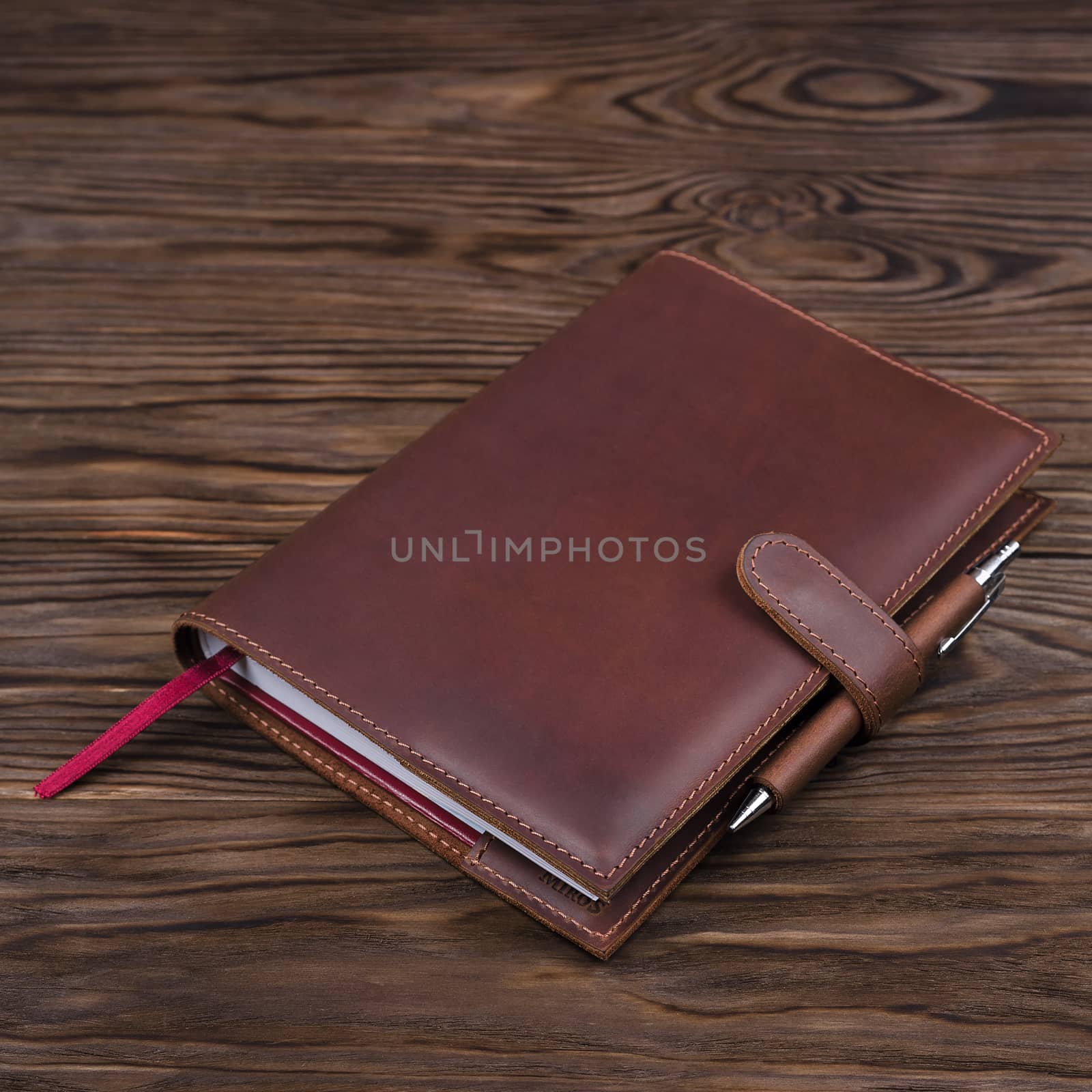 Red color handmade leather notebook cover with notebook and pen inside on wooden background. Stock photo of luxury business accessories. by alexsdriver