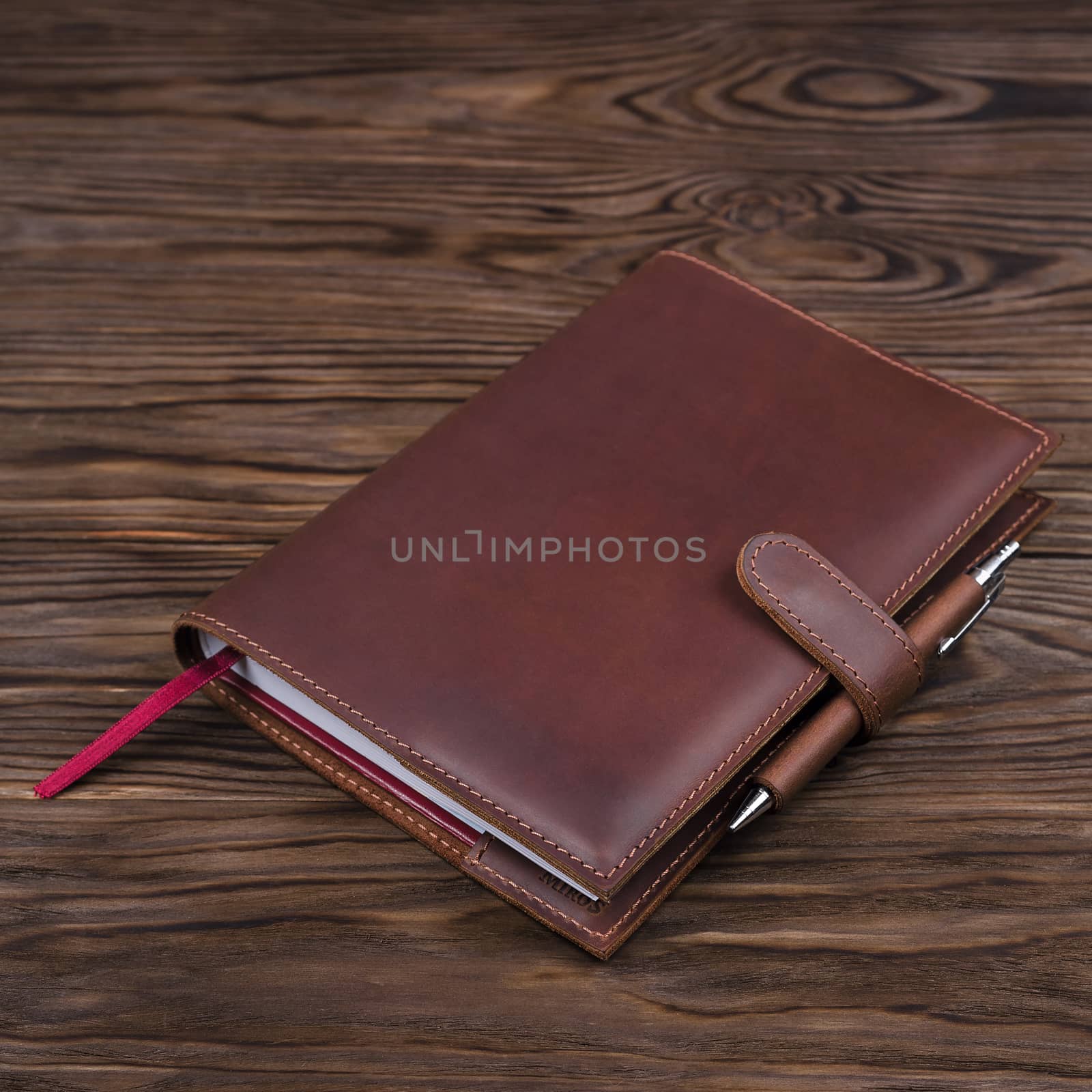 Red color handmade leather notebook cover with notebook and pen inside on wooden background. Stock photo of luxury business accessories.