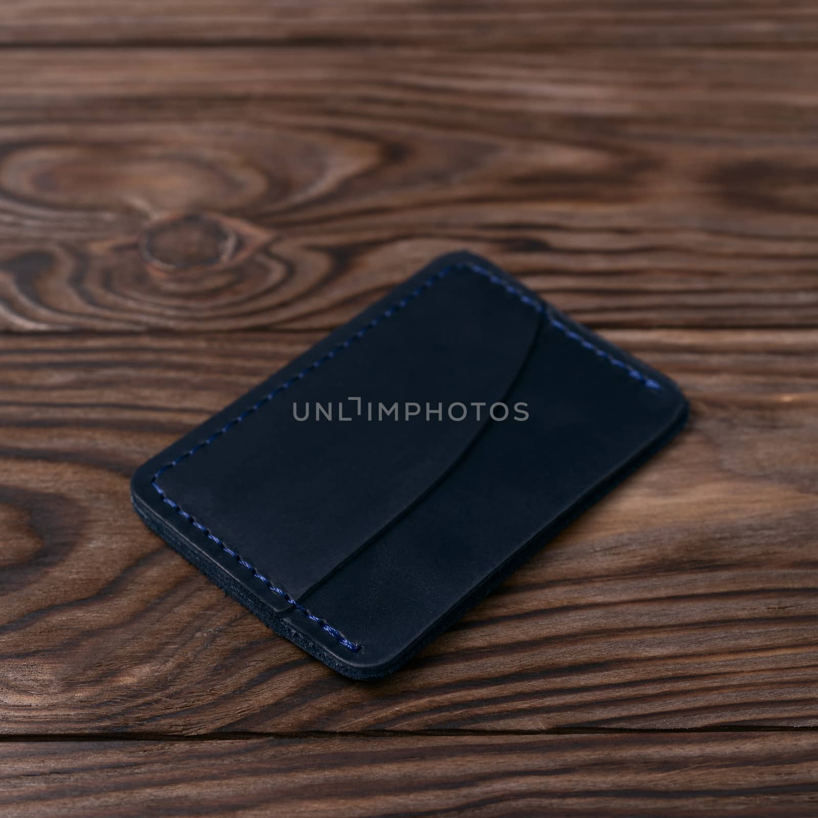 Blue colour handmade leather one pocket cardholder on wooden background. Stock photo with soft blurred background.