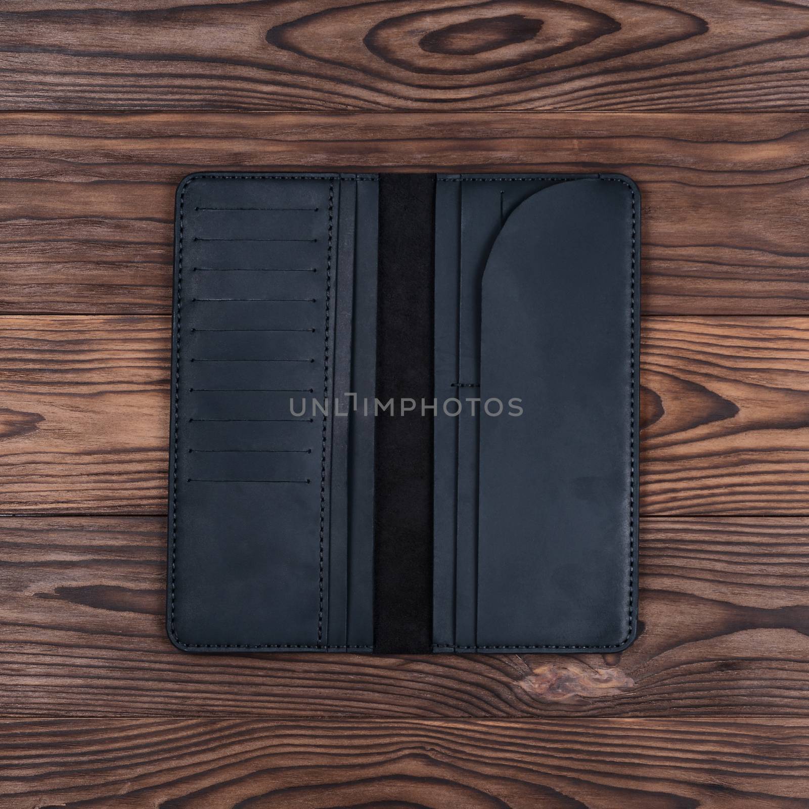 Handmade black travel wallet lies on textured wooden backgroud closeup. Wallet is open and empty. Up to down view. Stock photo of businessman accessories. by alexsdriver