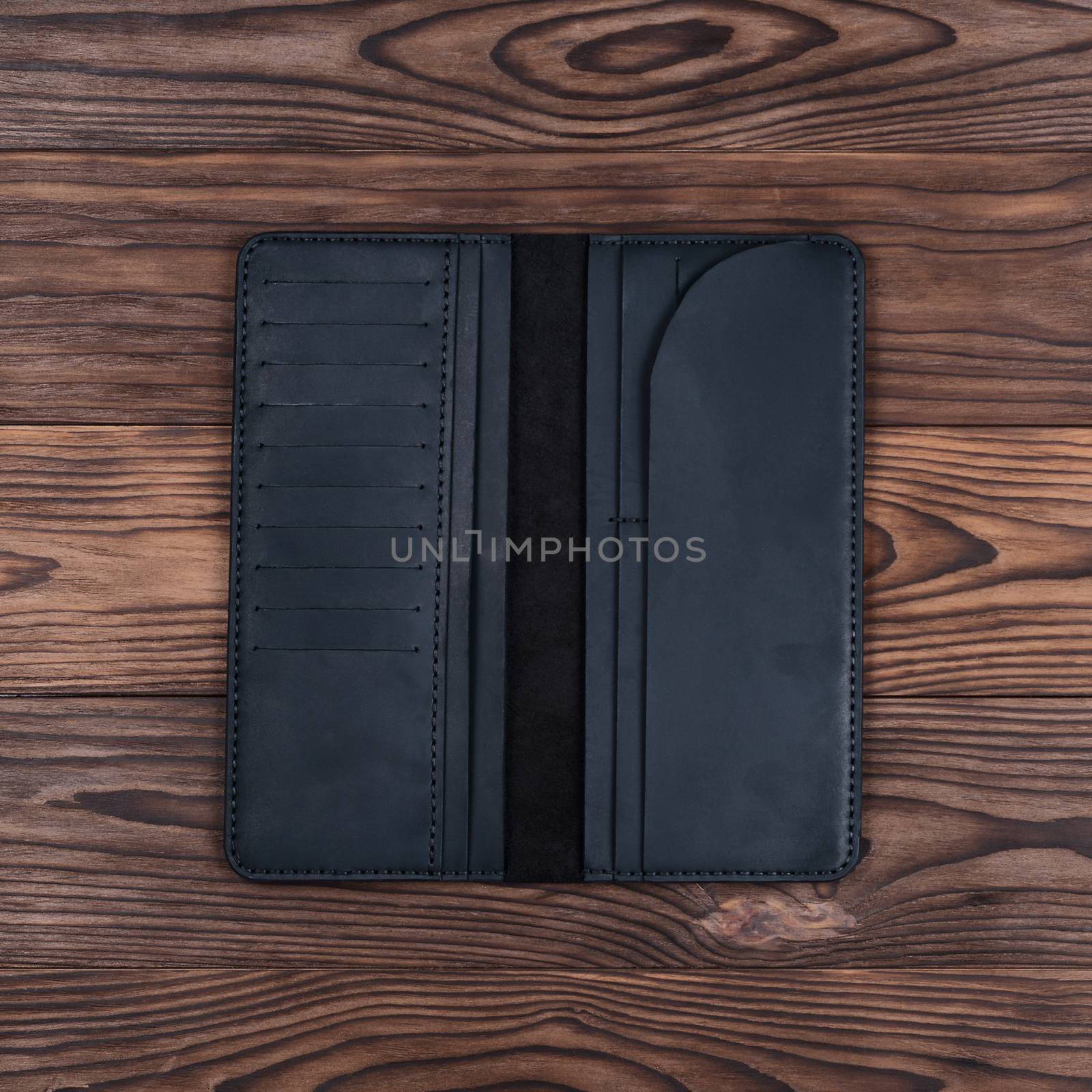 Handmade black travel wallet lies on textured wooden backgroud closeup. Wallet is open and empty. Up to down view. Stock photo of businessman accessories.