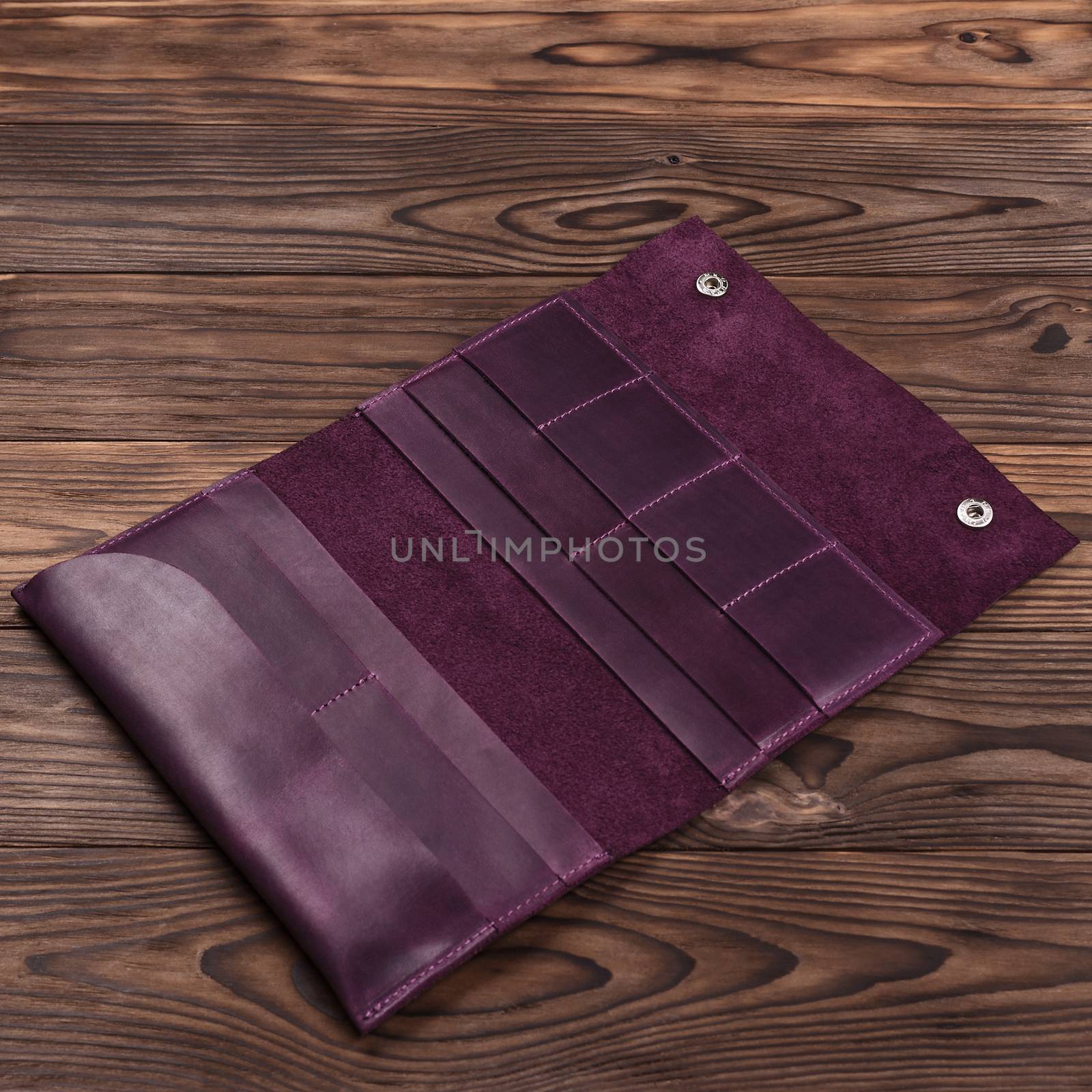 Handmade purple travel wallet lies on textured wooden backgroud closeup. Wallet is open and empty. Side view. Stock photo of businessman accessories.