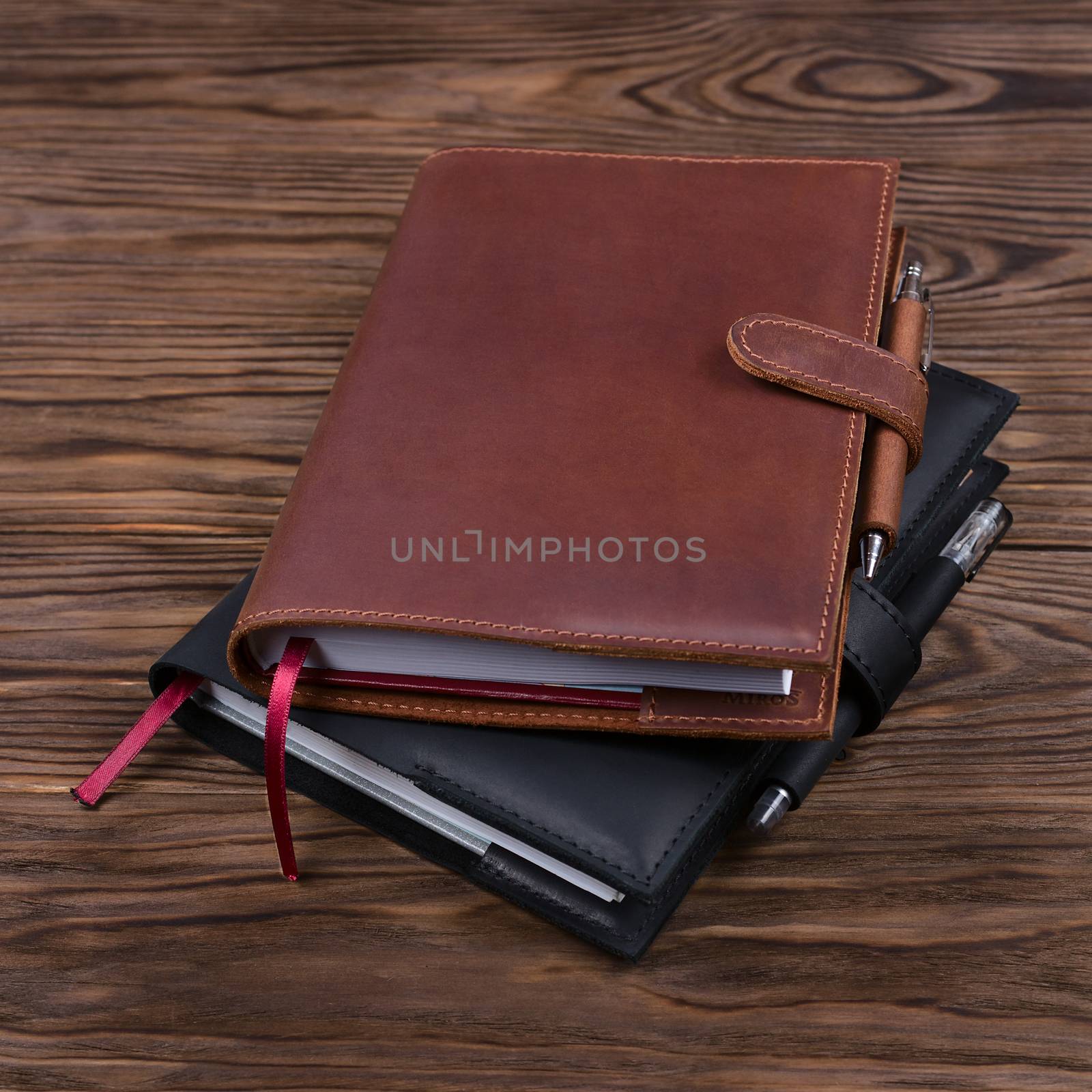 Brown and black handmade leather notebook covers with notebook and pen inside on wooden background. Stock photo of luxury business accessories.