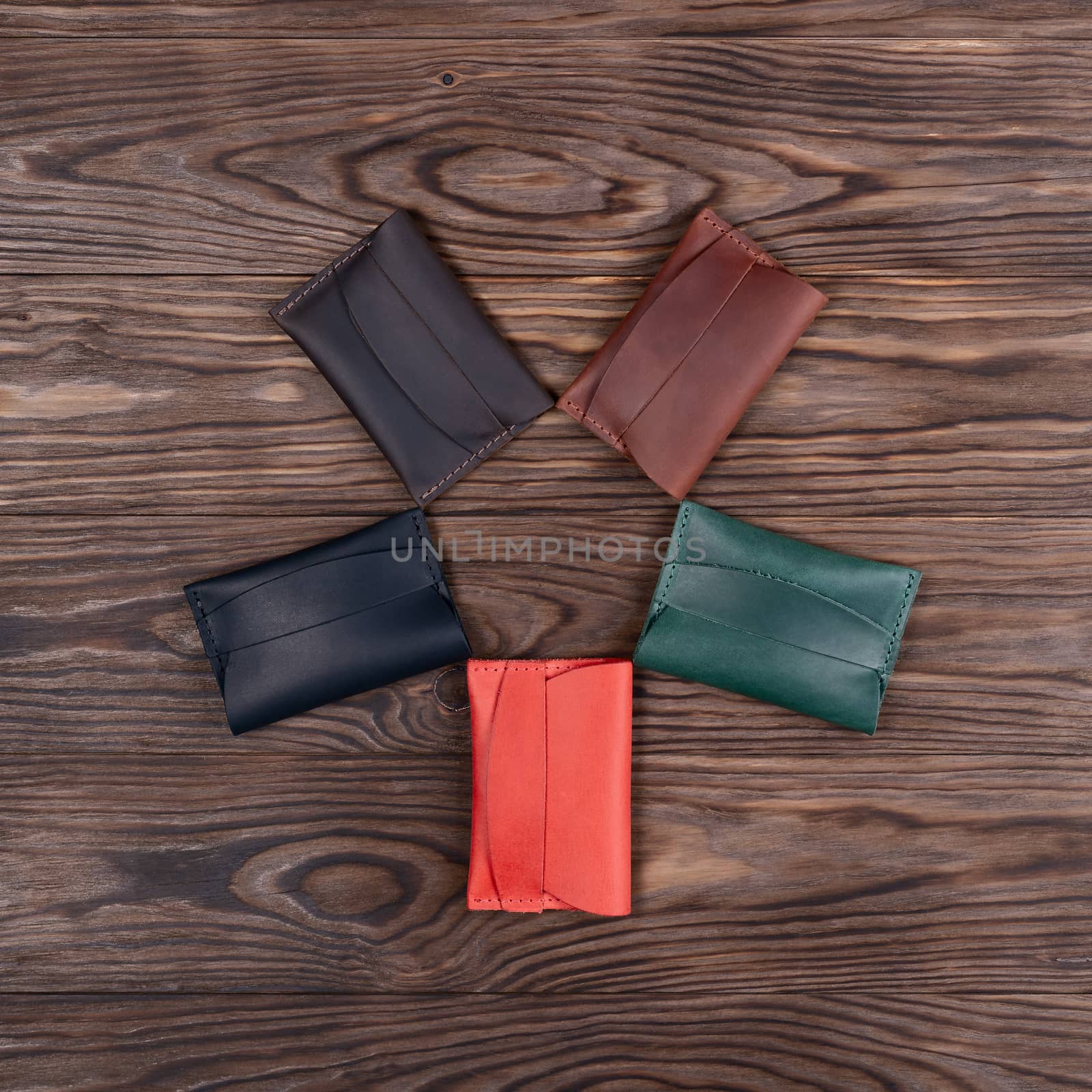 Flat lay photo of five different colour handmade leather one pocket cardholders. Red, black, blown, ginger and green colors. Stock photo on wooden background.