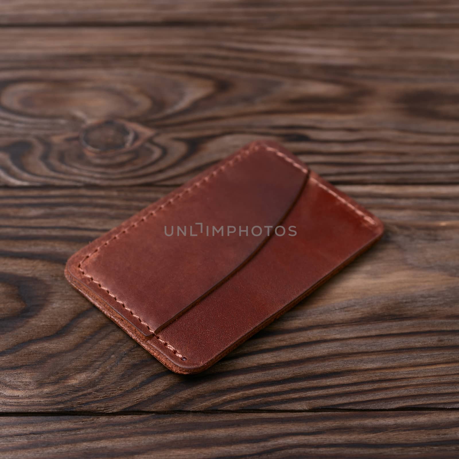 Ginger colour handmade leather one pocket cardholder on wooden background. Stock photo with soft blurred background.