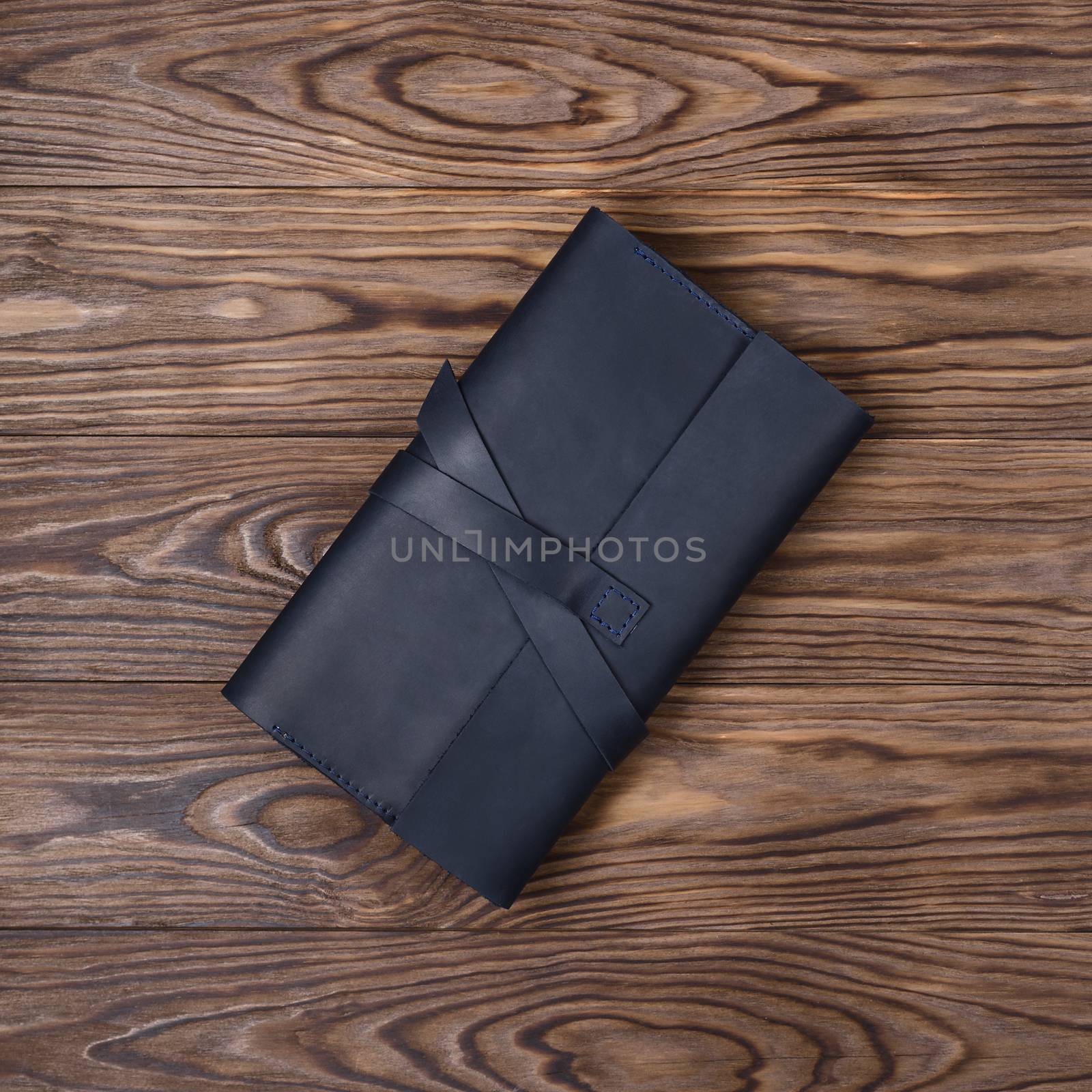 Black handmade travel wallet lies on textured wooden backgroud. Up to down view. Stock photo of businessman accessories.