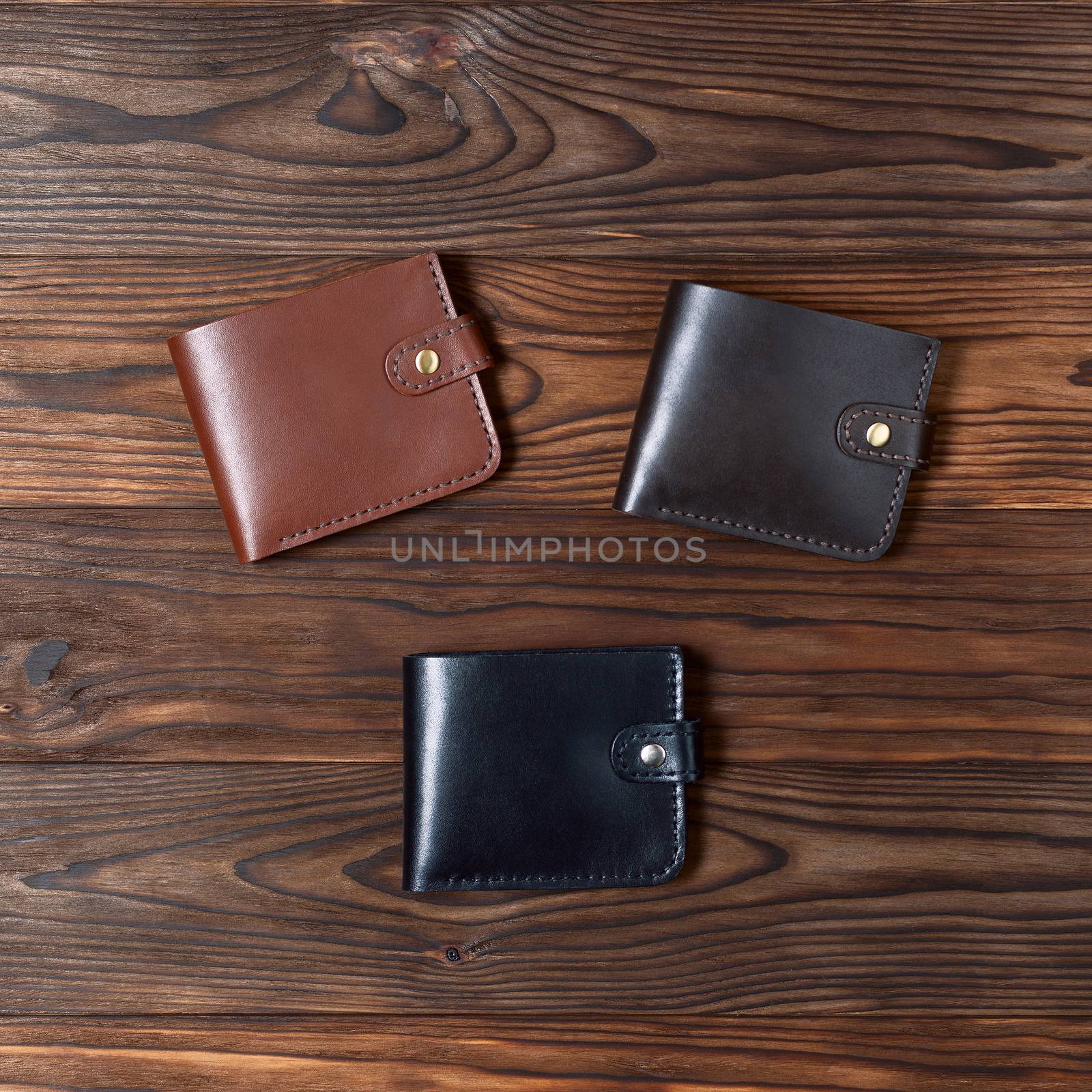 Three handmade leather gloss wallets on wooden textured background. Up to down view. Businessman wallet stock photo.