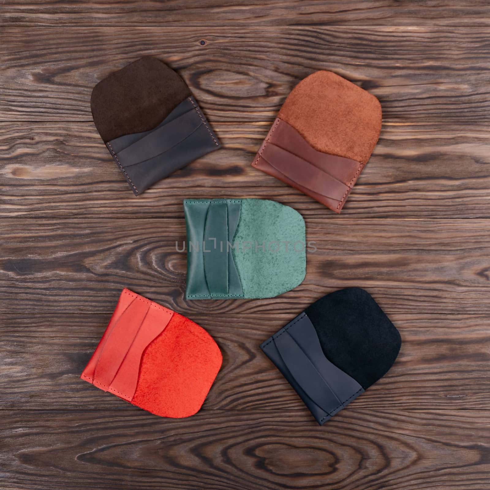 Flat lay photo of five different colour handmade leather one pocket cardholders.  Red, black, blown, ginger and green colors. Stock photo on wooden background.