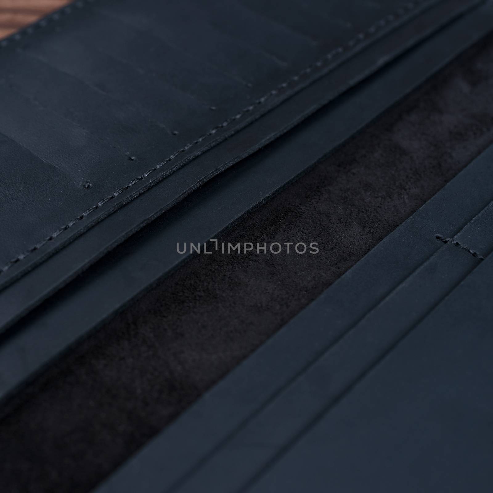 Part of handmade black travel wallet lies on textured wooden backgroud closeup. Wallet is open and empty. Side view. Stock photo of businessman accessories.