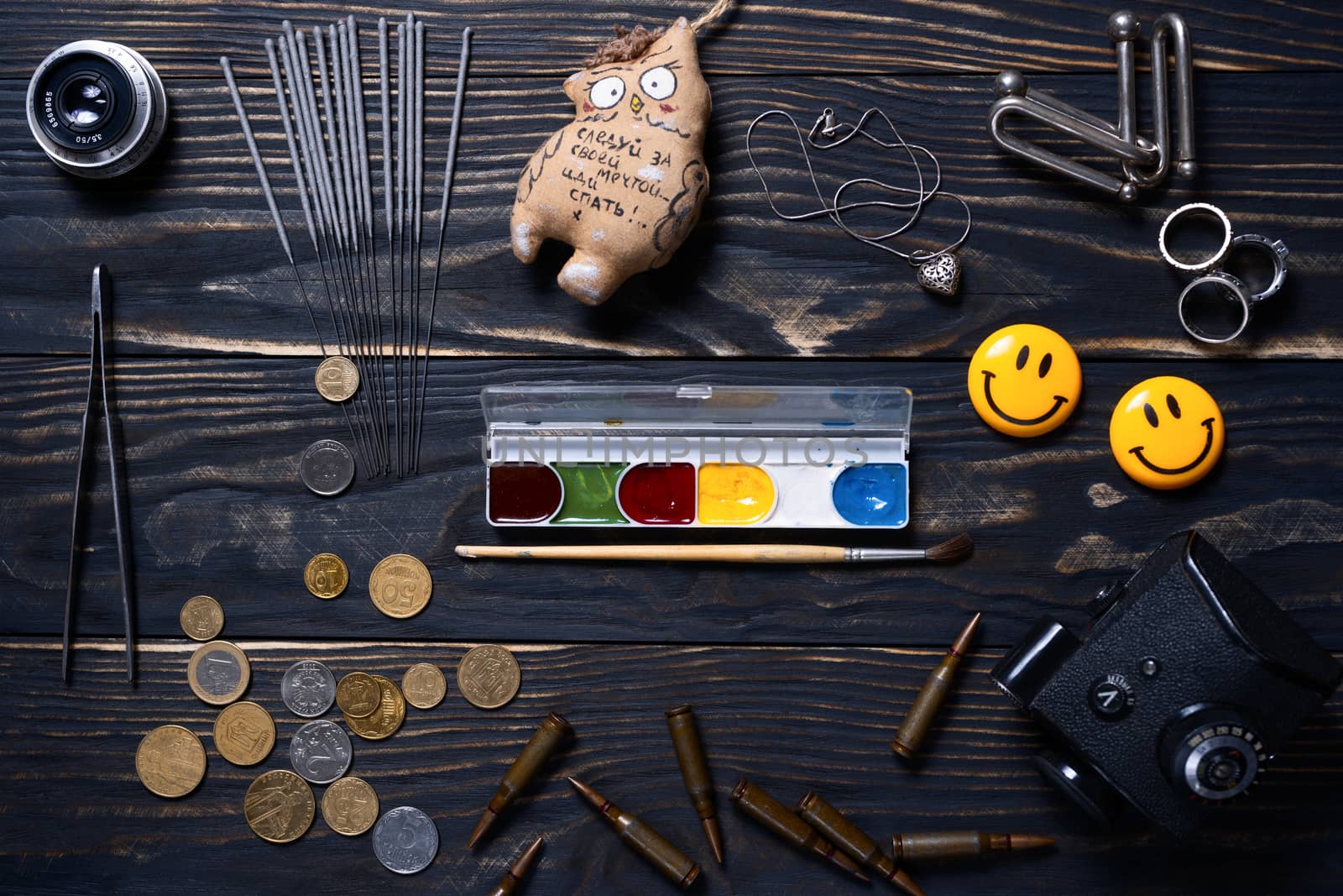 Flat lay wooden charred background. On wooden boards lies bengali fire, silver pendant, tweezers, toy, rings, coins, brush and paint, ammo, smiling magnets, camera prism and old lens.