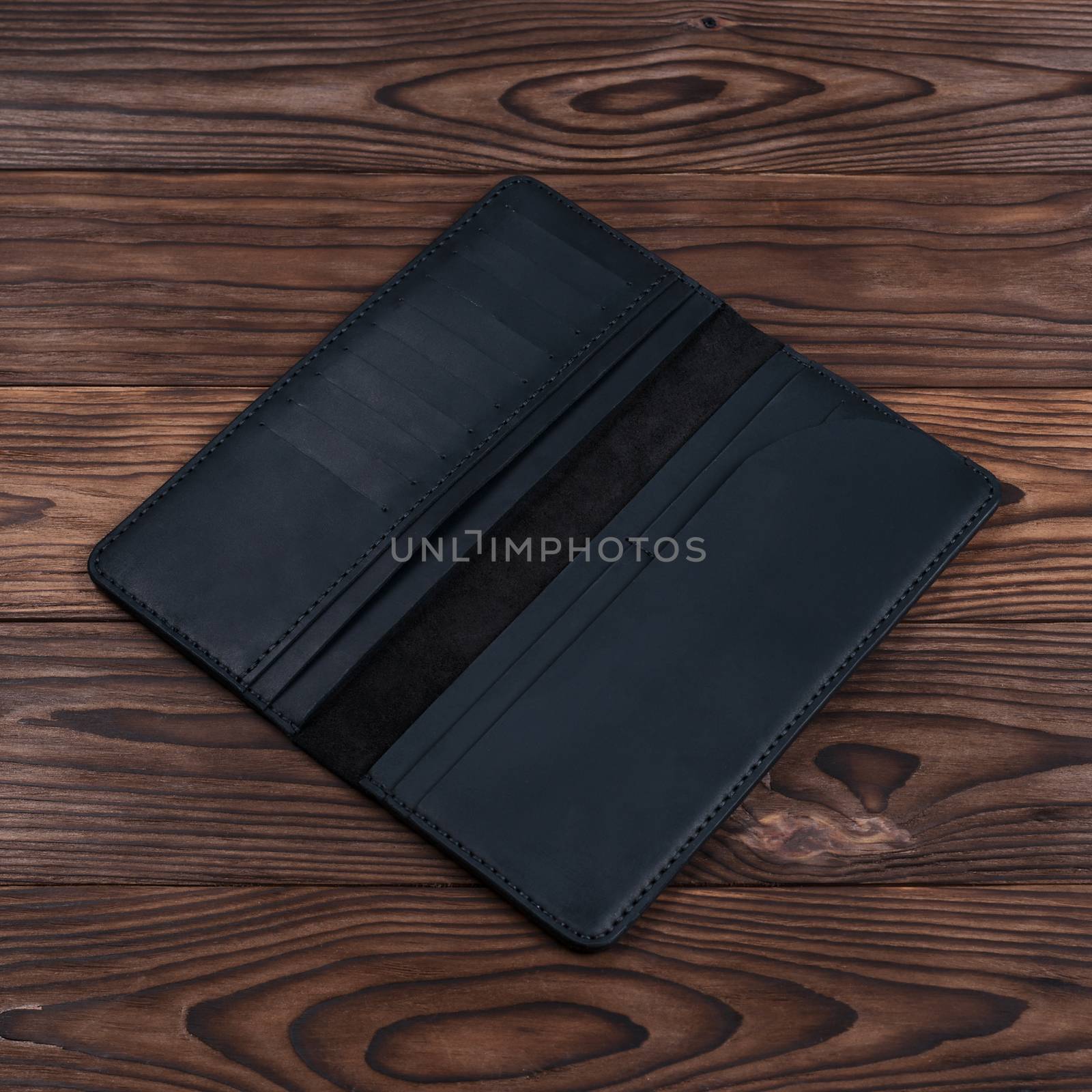 Handmade black travel wallet lies on textured wooden backgroud closeup. Wallet is open and empty. Side view. Stock photo of businessman accessories. by alexsdriver