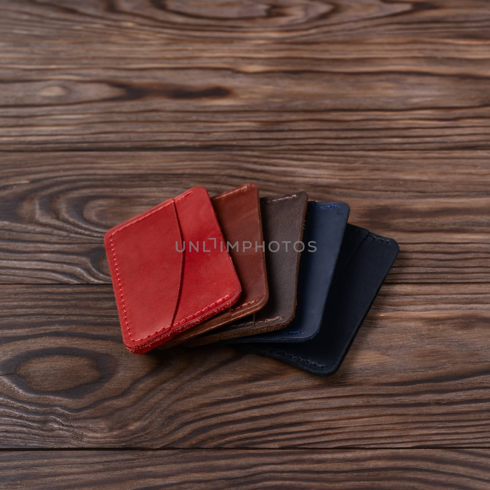 Five handmade leather cardholders on wooden background lie one on another. Stock photo with blurred background.