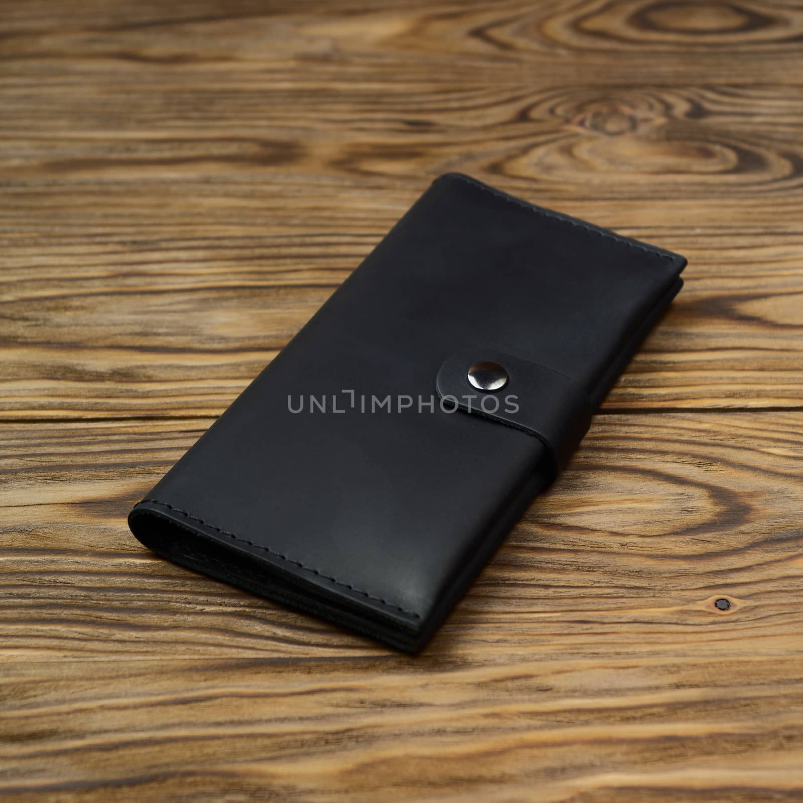 Black color handmade leather wallet on textured wooden background. Wallet is unisex. Side view. Stock photo of luxury accessories.