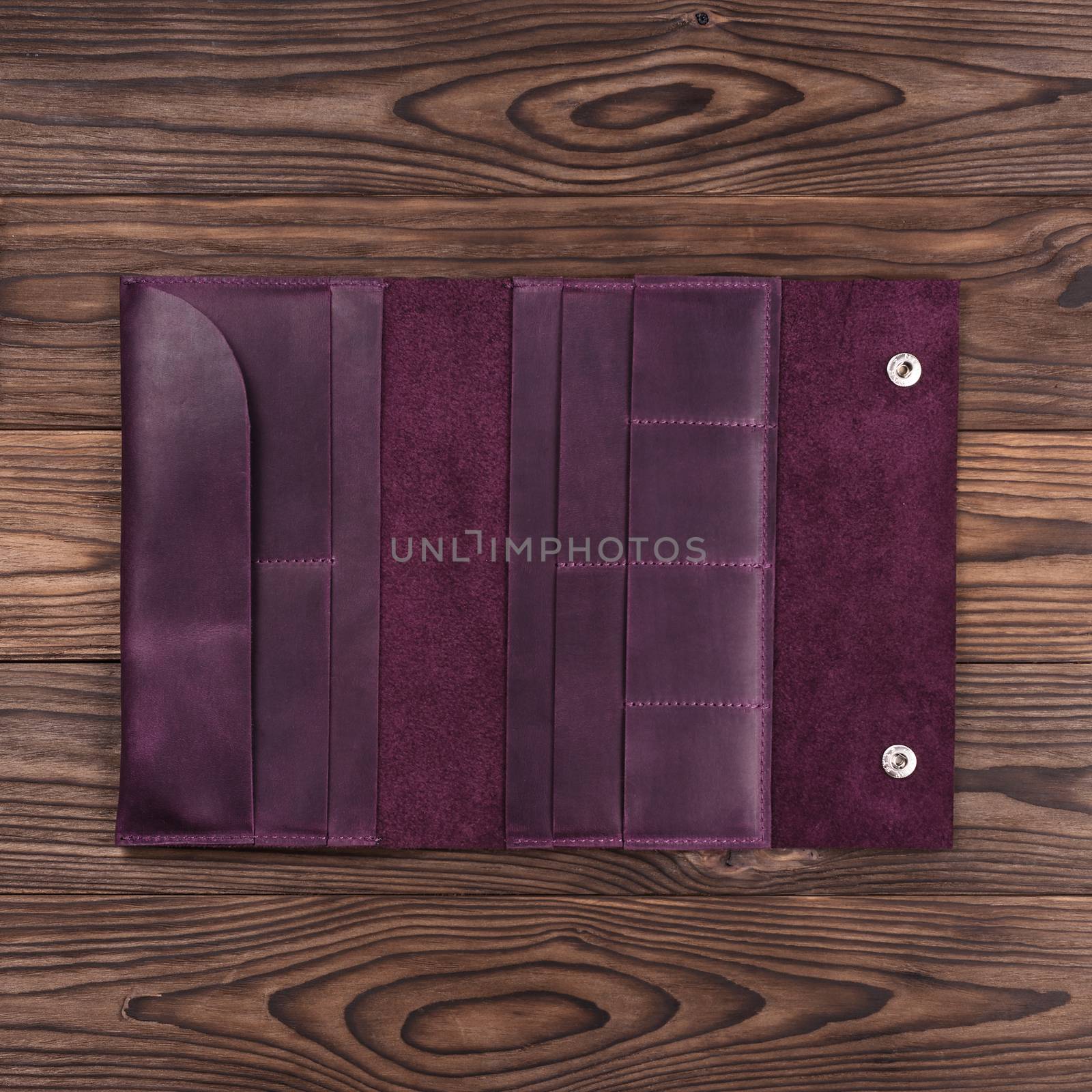 Purple handmade travel wallet lies on textured wooden backgroud closeup. Wallet is open and empty. Up to down view. Stock photo of businessman accessories.