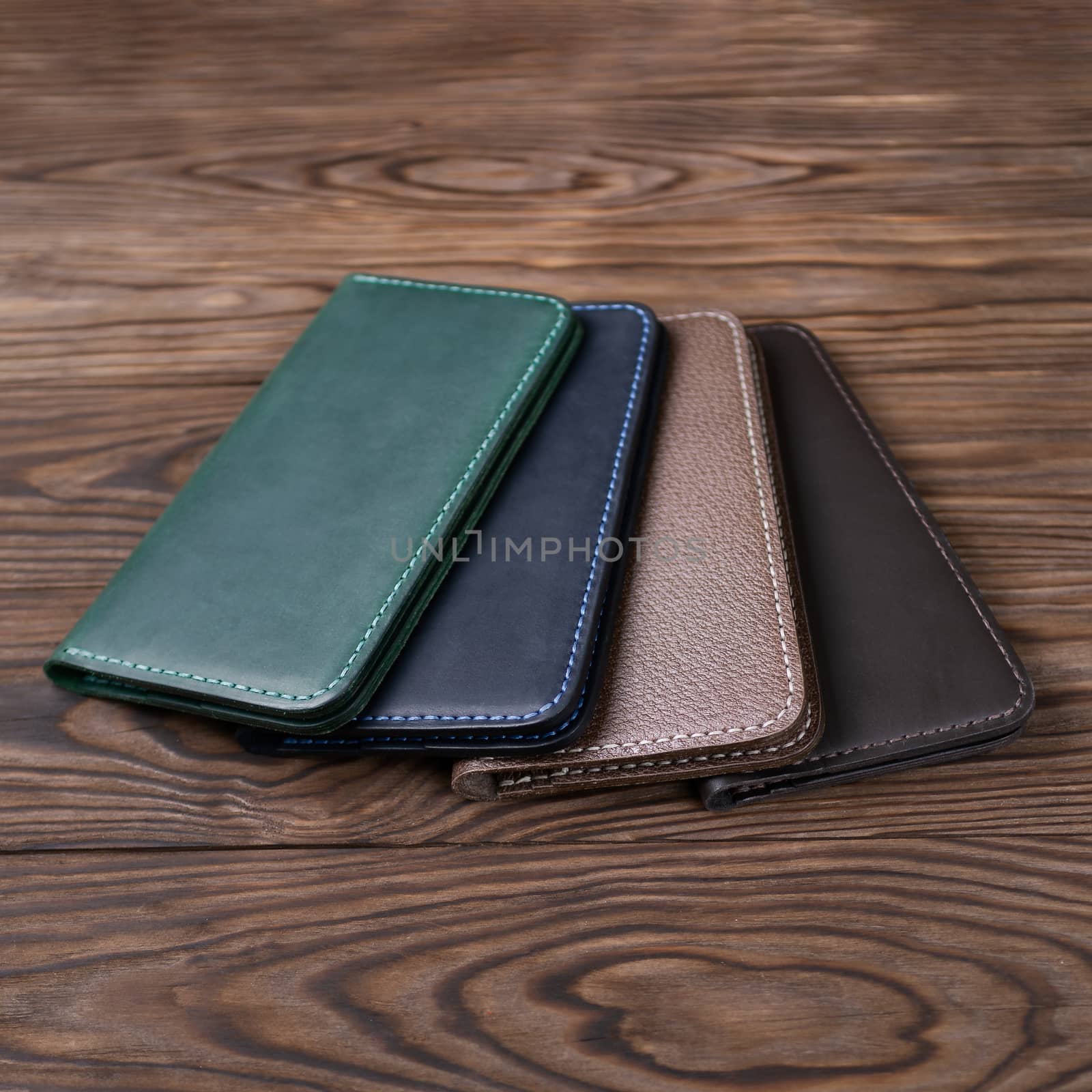 Four handmade leather porte-monnaie on wooden textured background. Side view. Stock photo of luxury accessories.