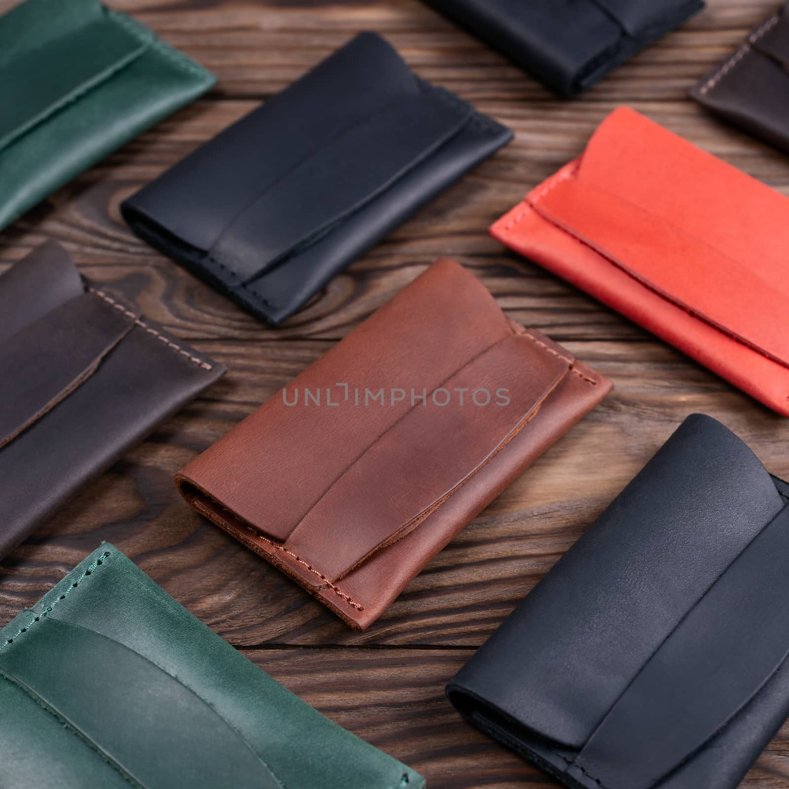 Flat lay photo of five different colour handmade leather one pocket cardholders. Red, black, blown, ginger and green colors. Stock photo on wooden background. by alexsdriver